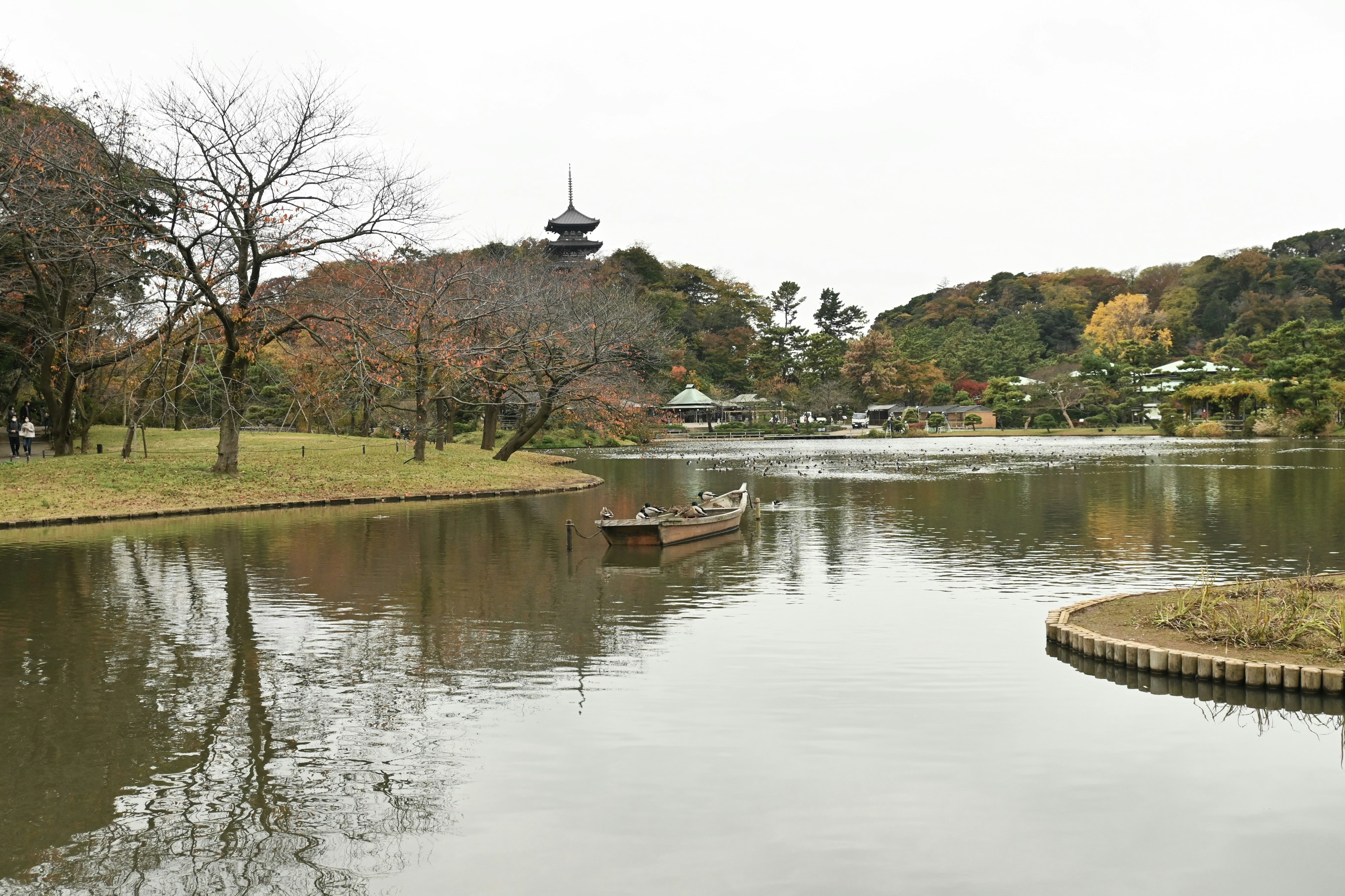 Pemandangan kolam yang tenang dengan perahu kecil melayang dan pagoda di kejauhan