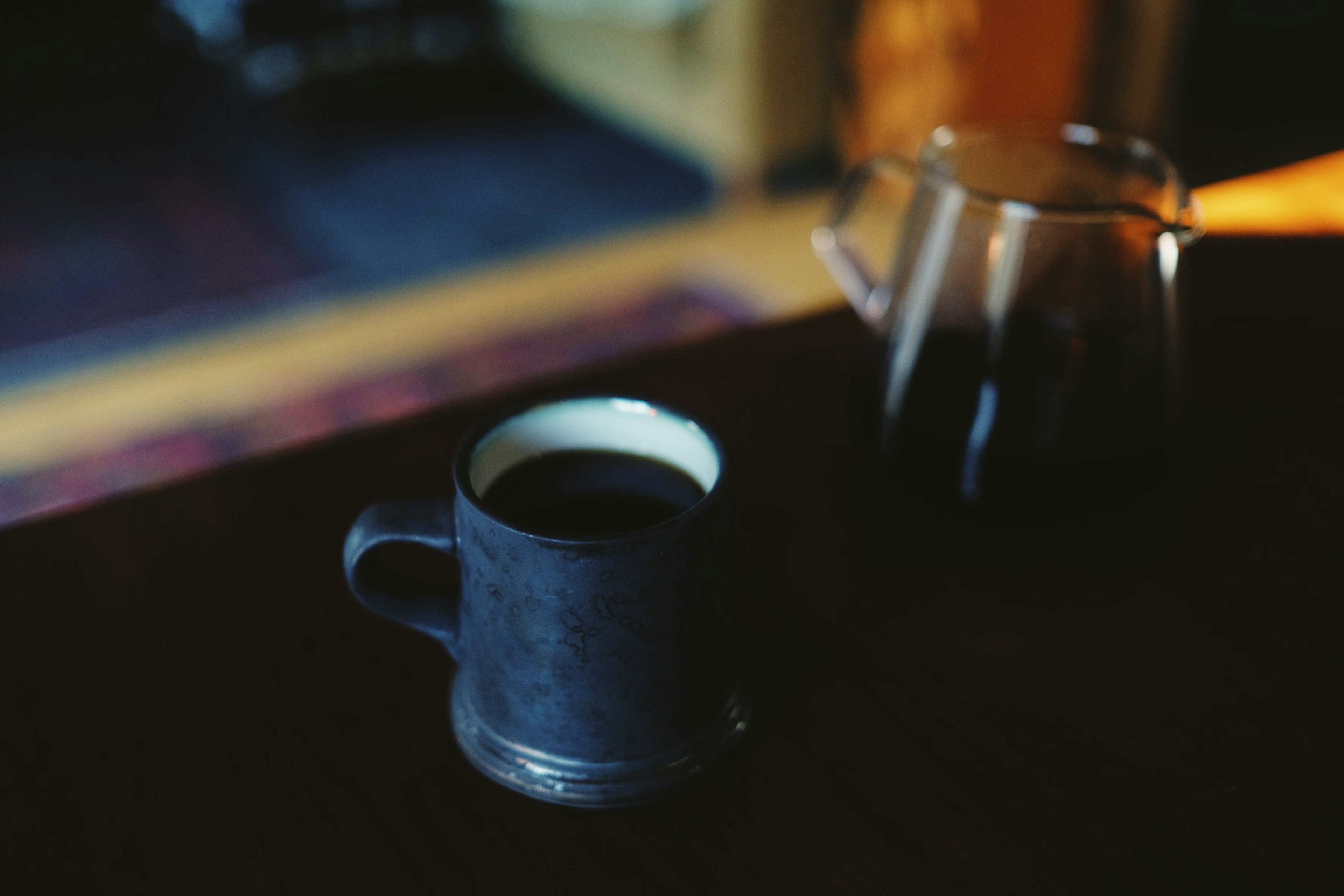 A black coffee cup next to a clear coffee pot on a wooden table