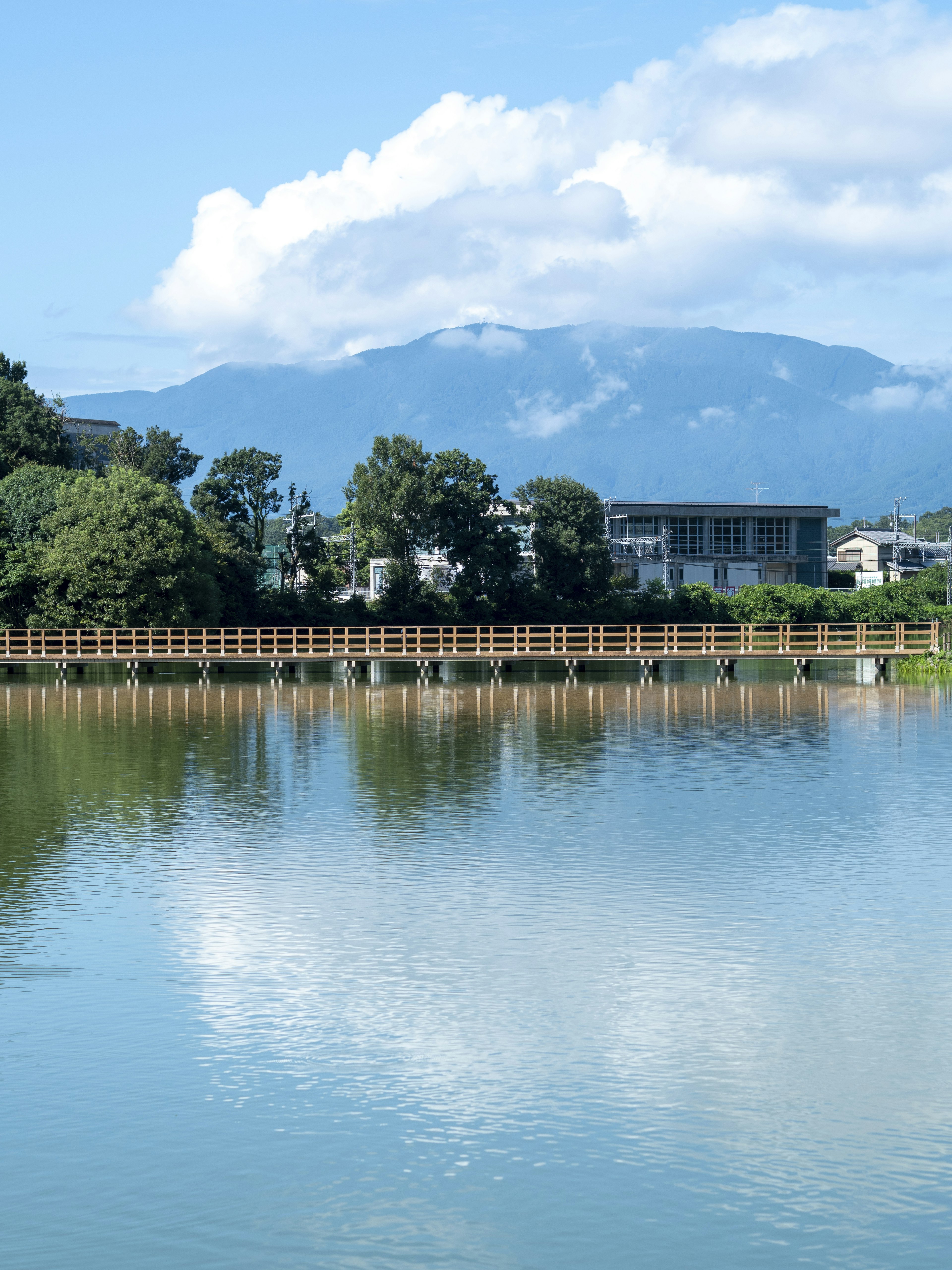 Ruhiger See, der den blauen Himmel und die weißen Wolken mit Bergen und Gebäuden im Hintergrund spiegelt