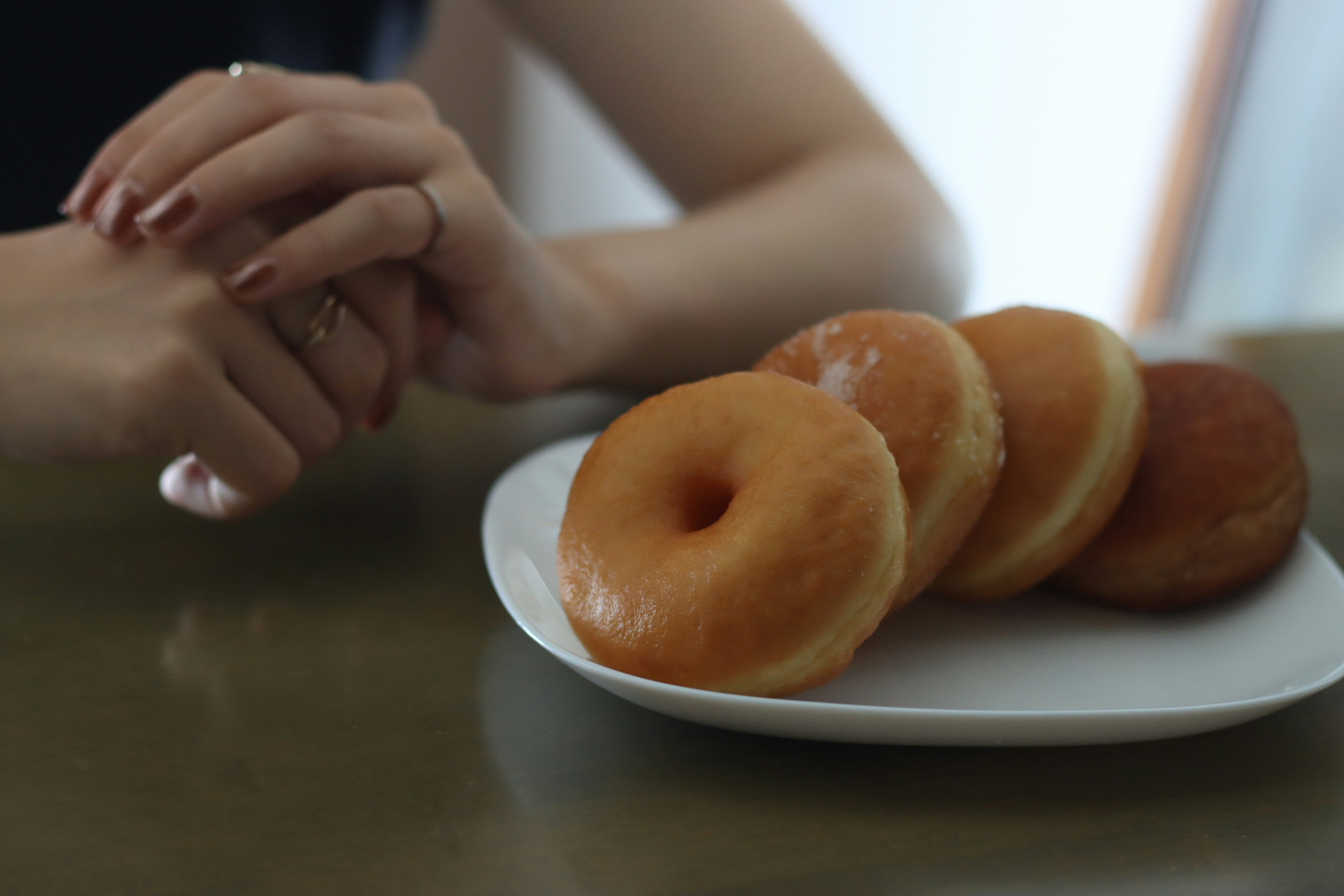 Hände ruhen neben einem Teller mit Donuts auf einem Tisch