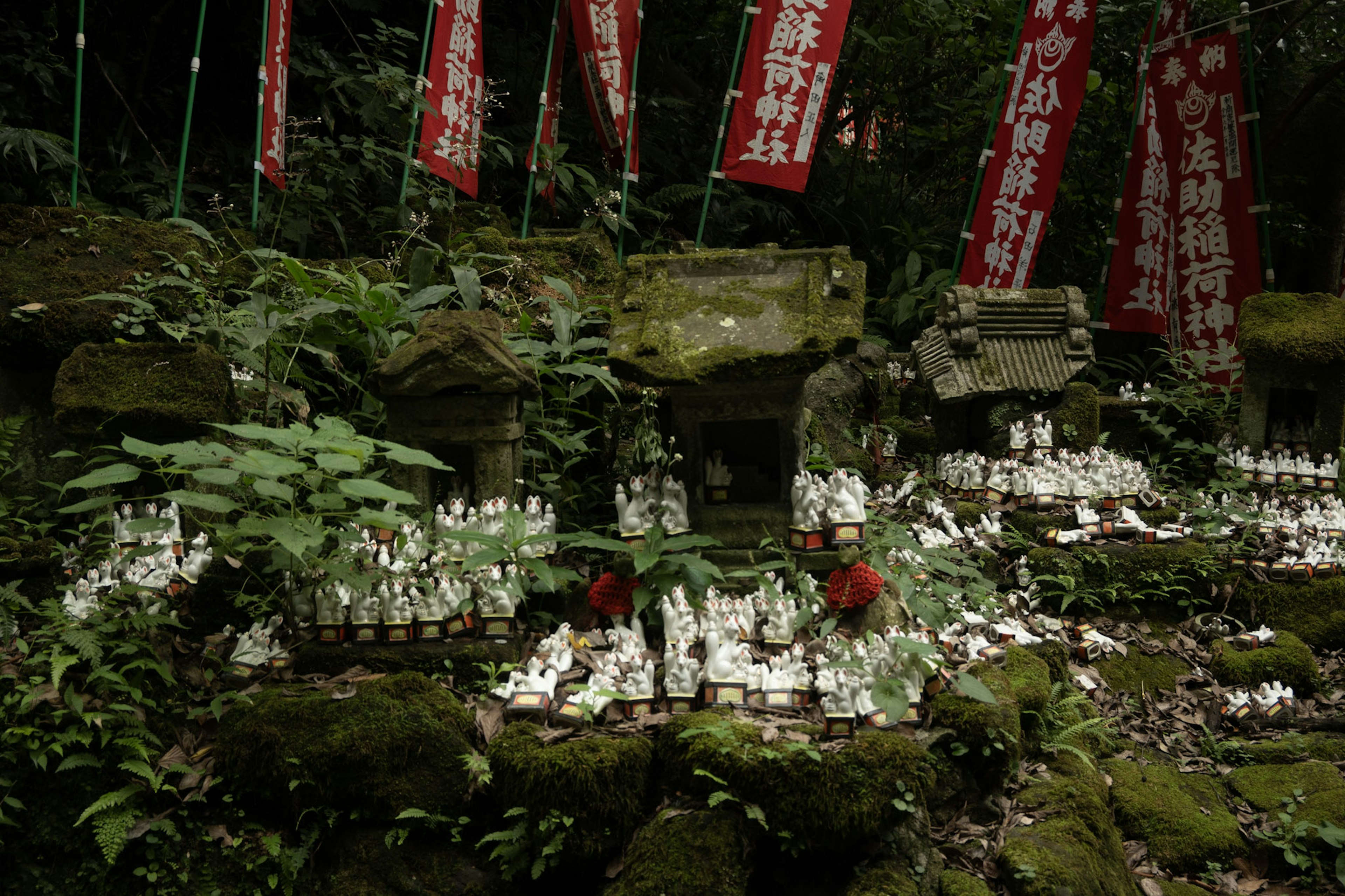 A lush scene featuring small white statues and red banners surrounding a shrine