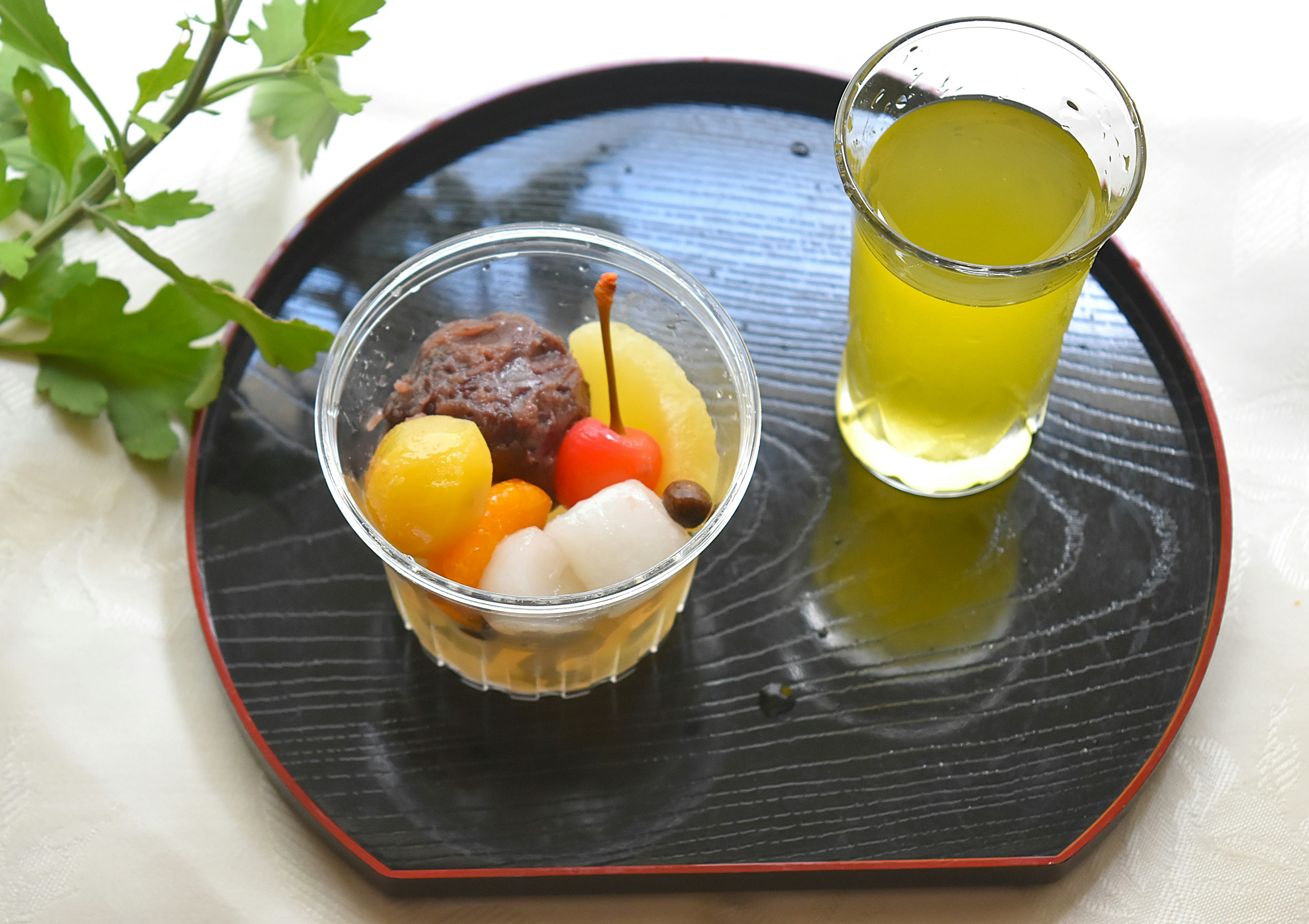 Dessert with fruits and traditional sweets in a clear cup alongside green tea