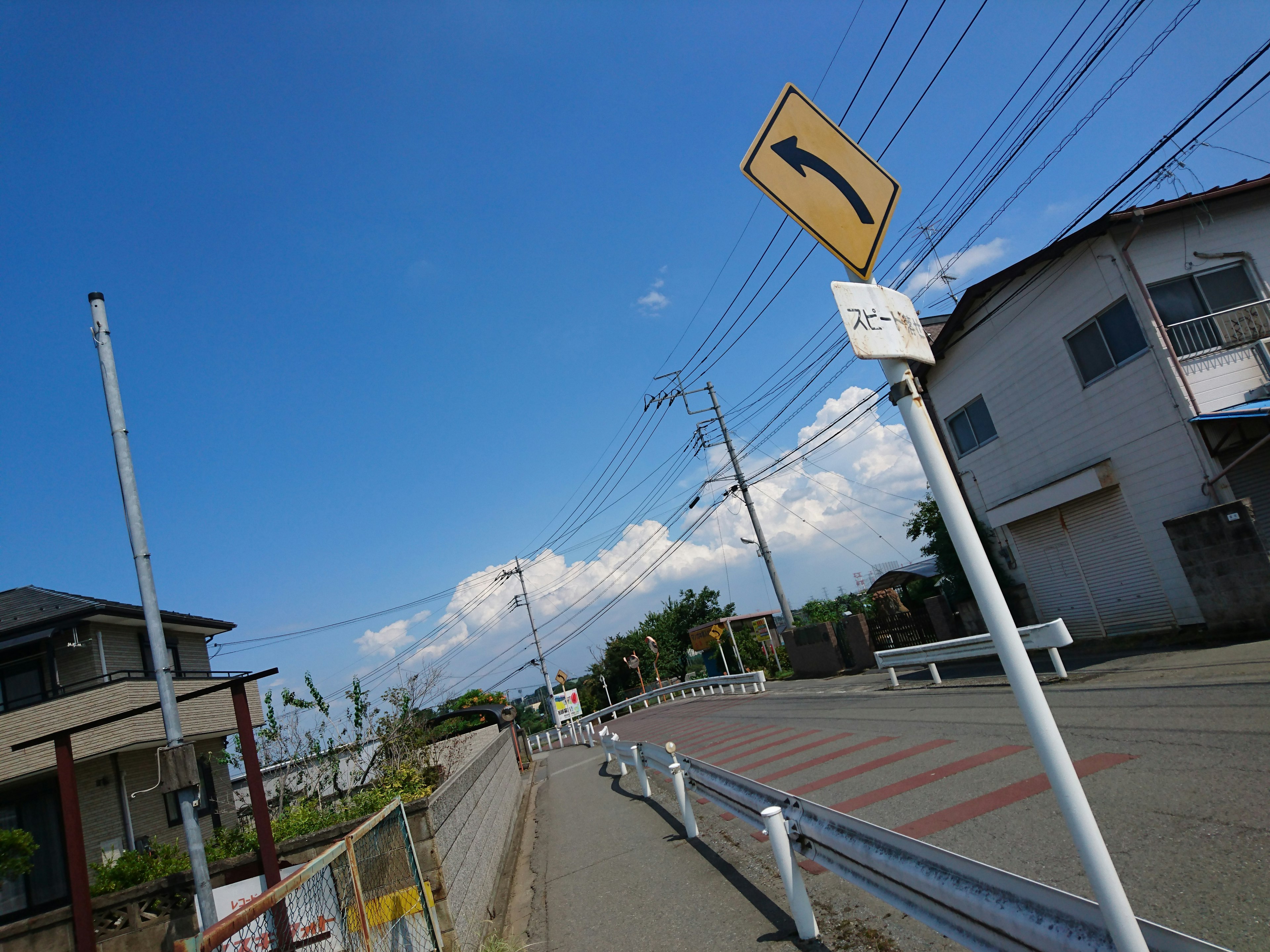 青空の下にある左折標識と住宅街の風景