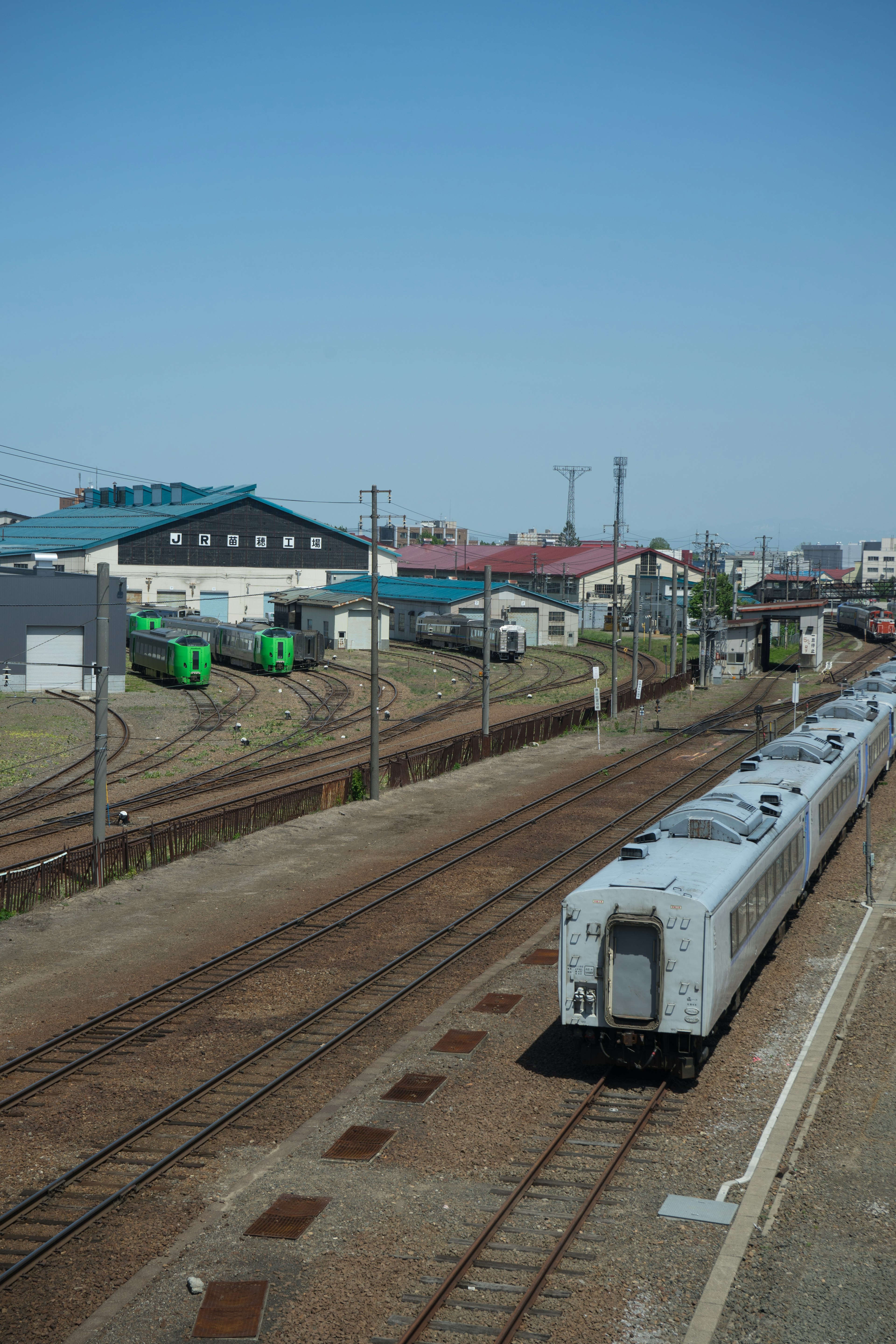 รางรถไฟและรถไฟพร้อมท้องฟ้าสีฟ้าสดใสและอาคารในพื้นหลัง