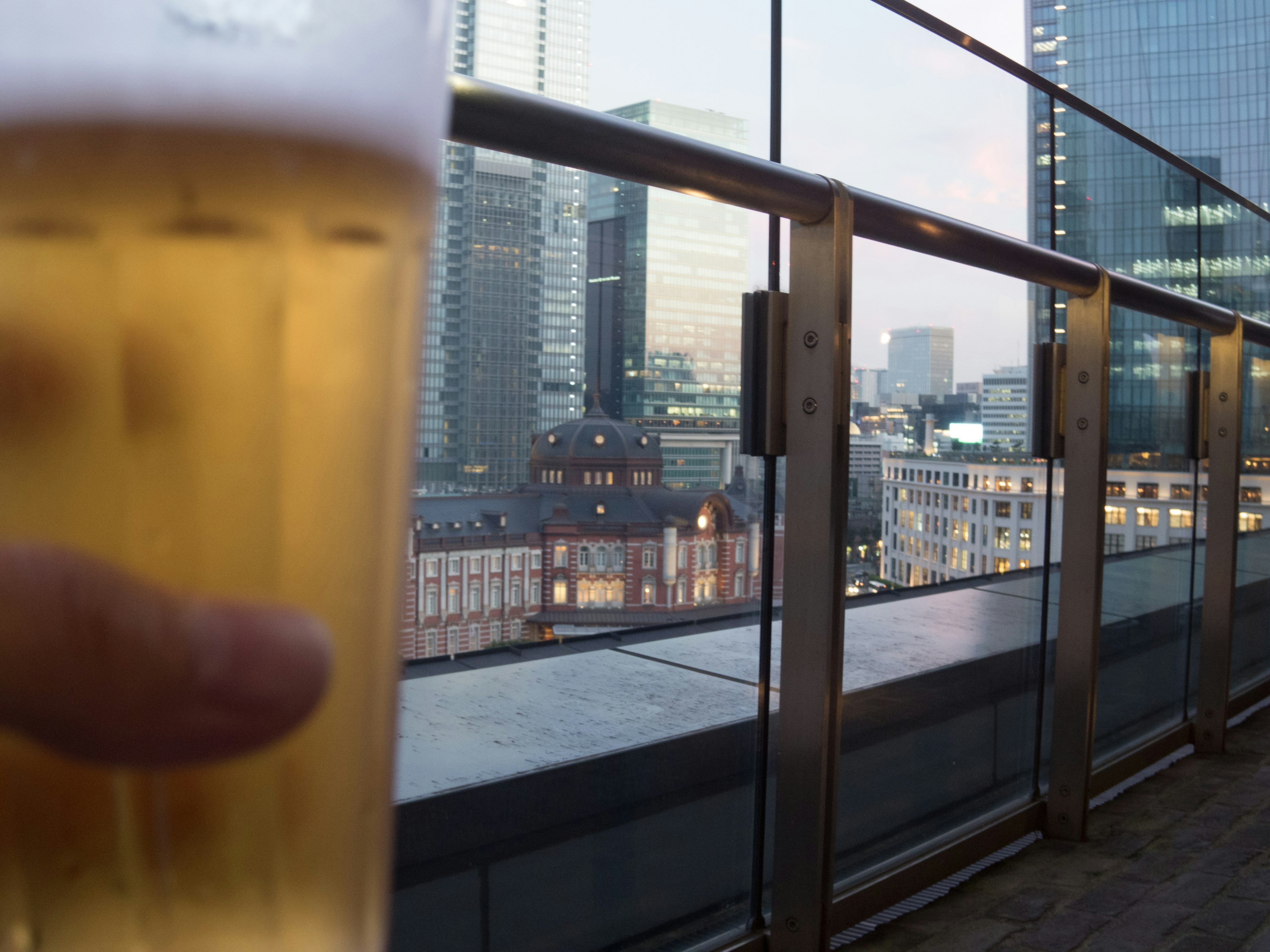 ビールを持つ手が映り込んだ屋上の風景 都市のスカイラインとガラスのビルが背景