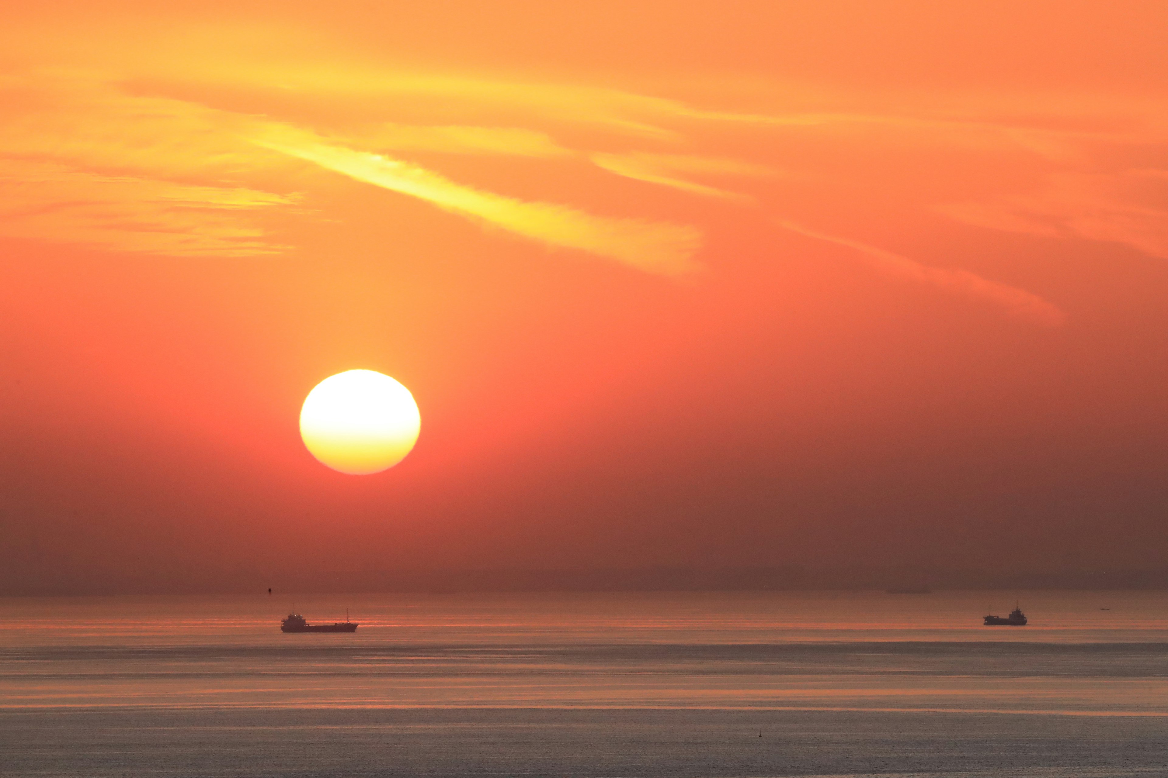 オレンジ色の夕日が海の上に沈んでいるシーン 船が二隻浮かんでいる