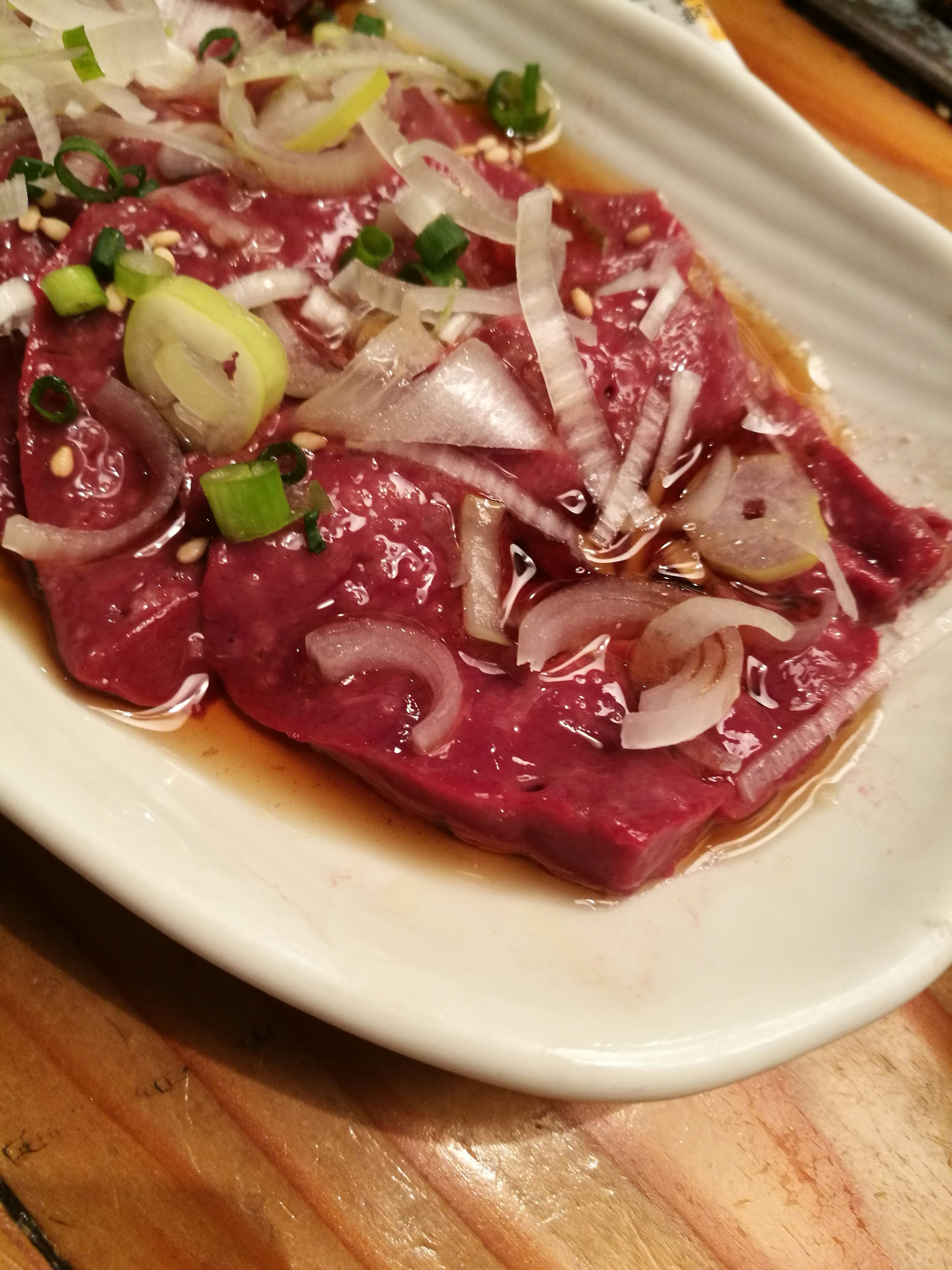 Sliced meat topped with green onions and shallots on a plate