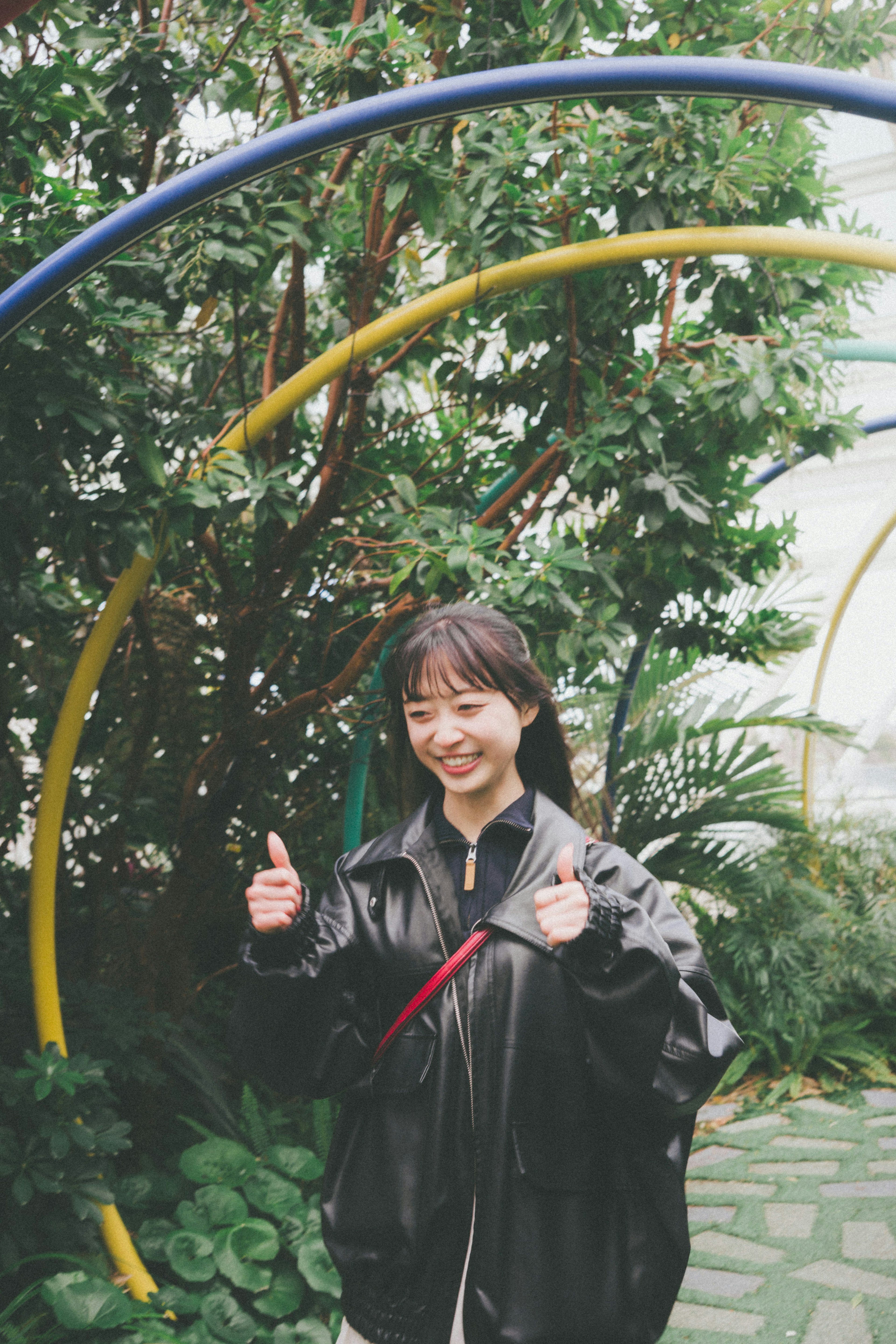 A woman giving a thumbs up surrounded by greenery and colorful arches