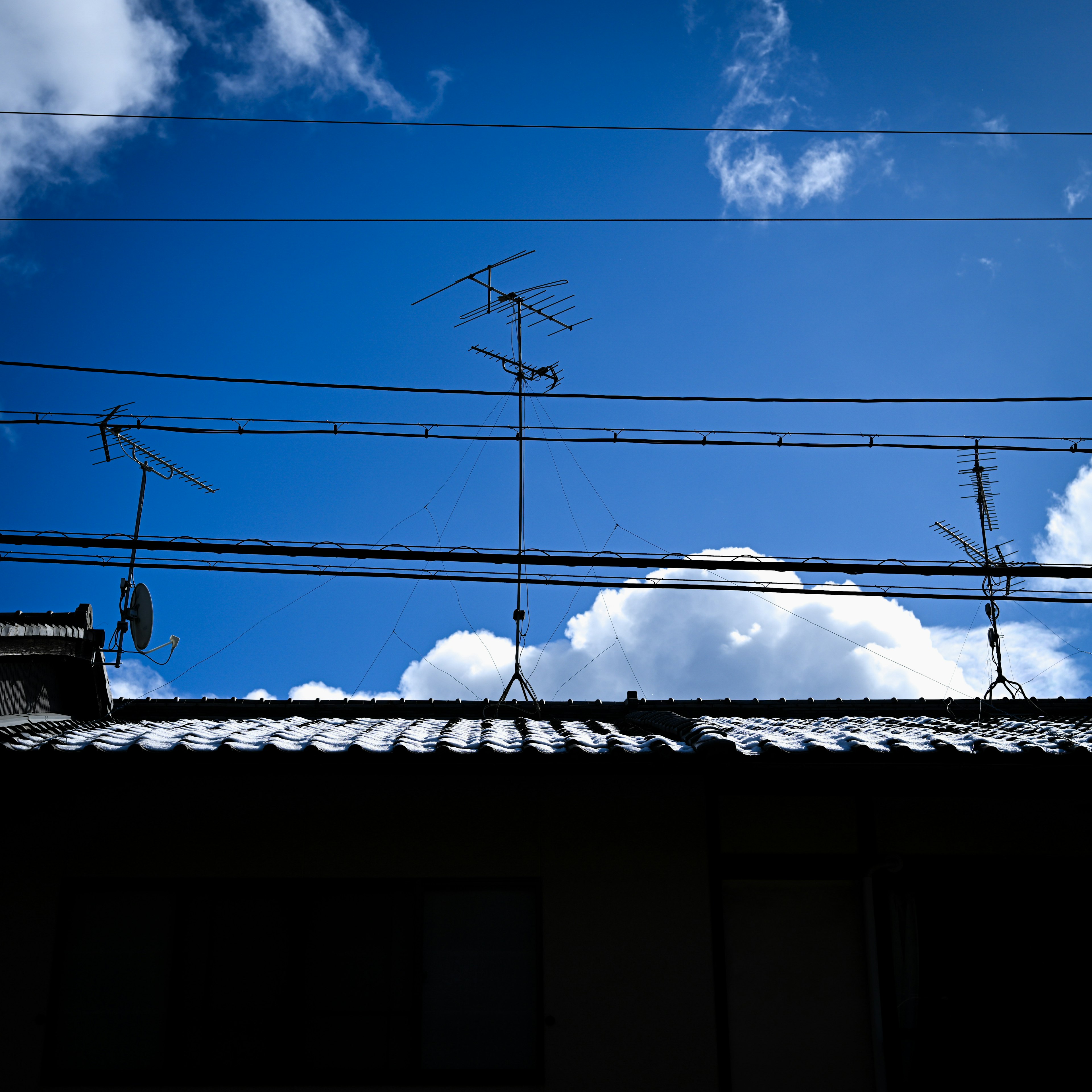 Une vue d'un toit de maison et de fils électriques contre un ciel bleu avec des nuages blancs