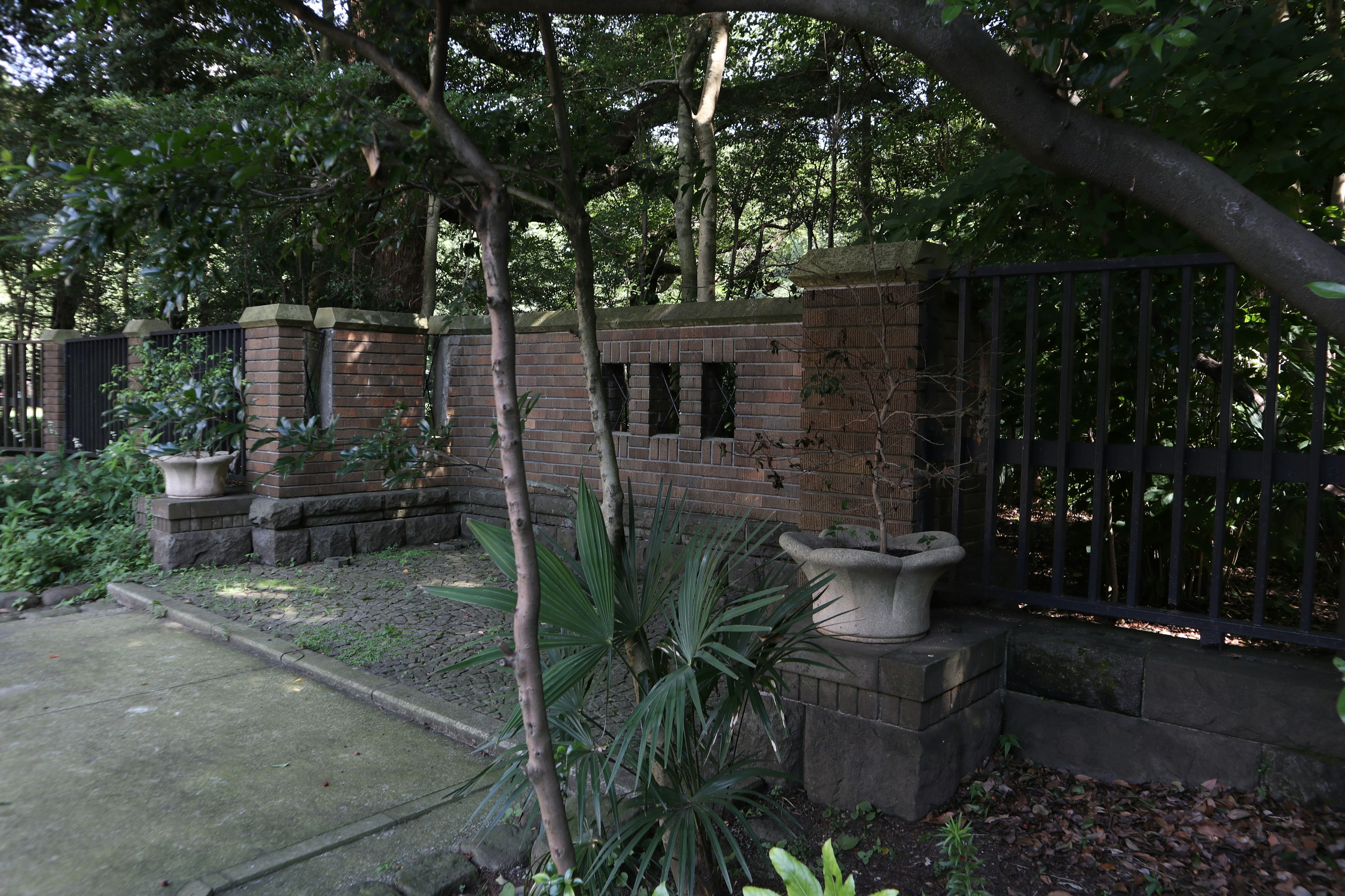 Old brick wall and iron fence surrounded by lush greenery in a garden