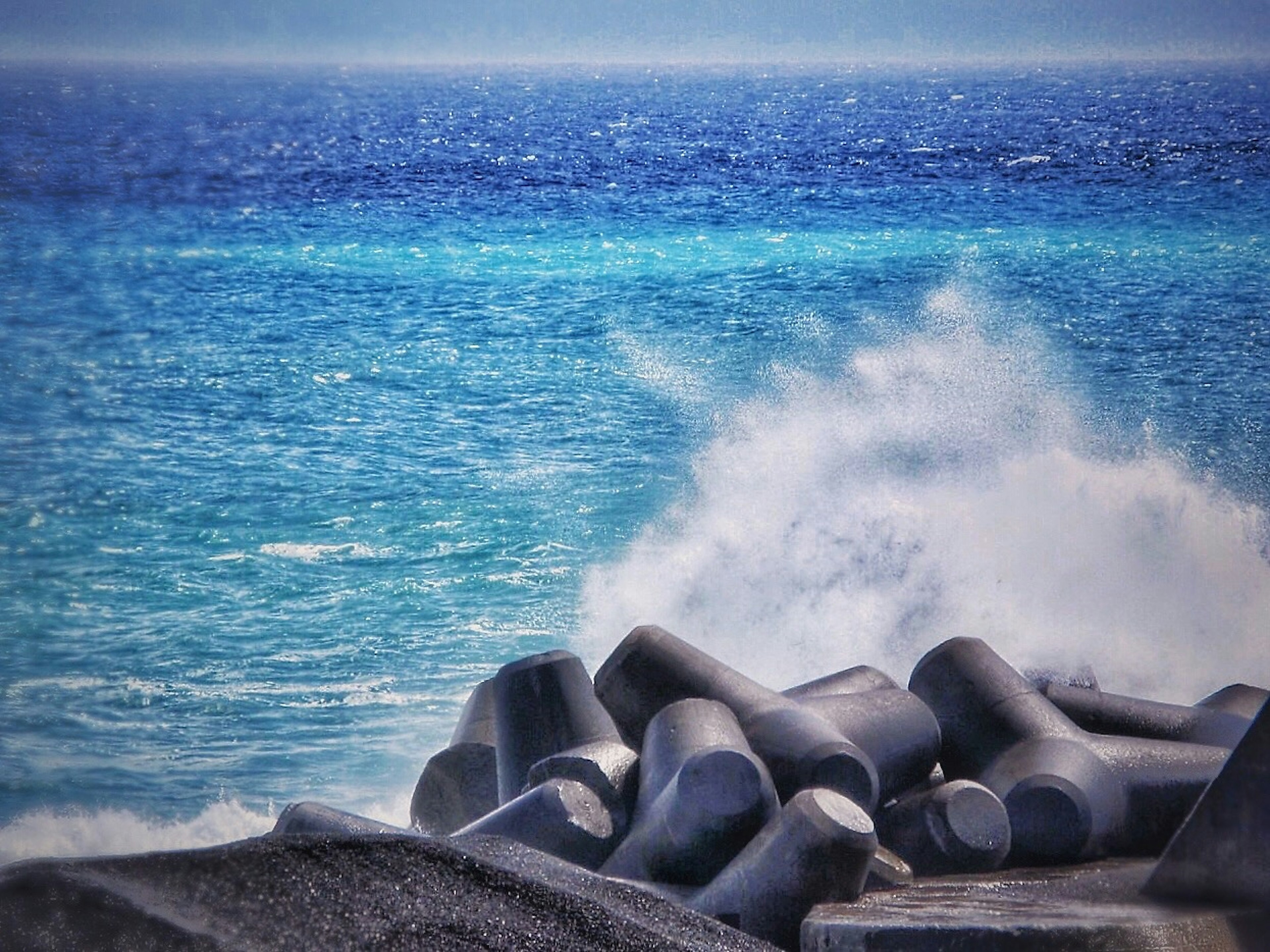 Waves crashing against large concrete blocks by the blue sea