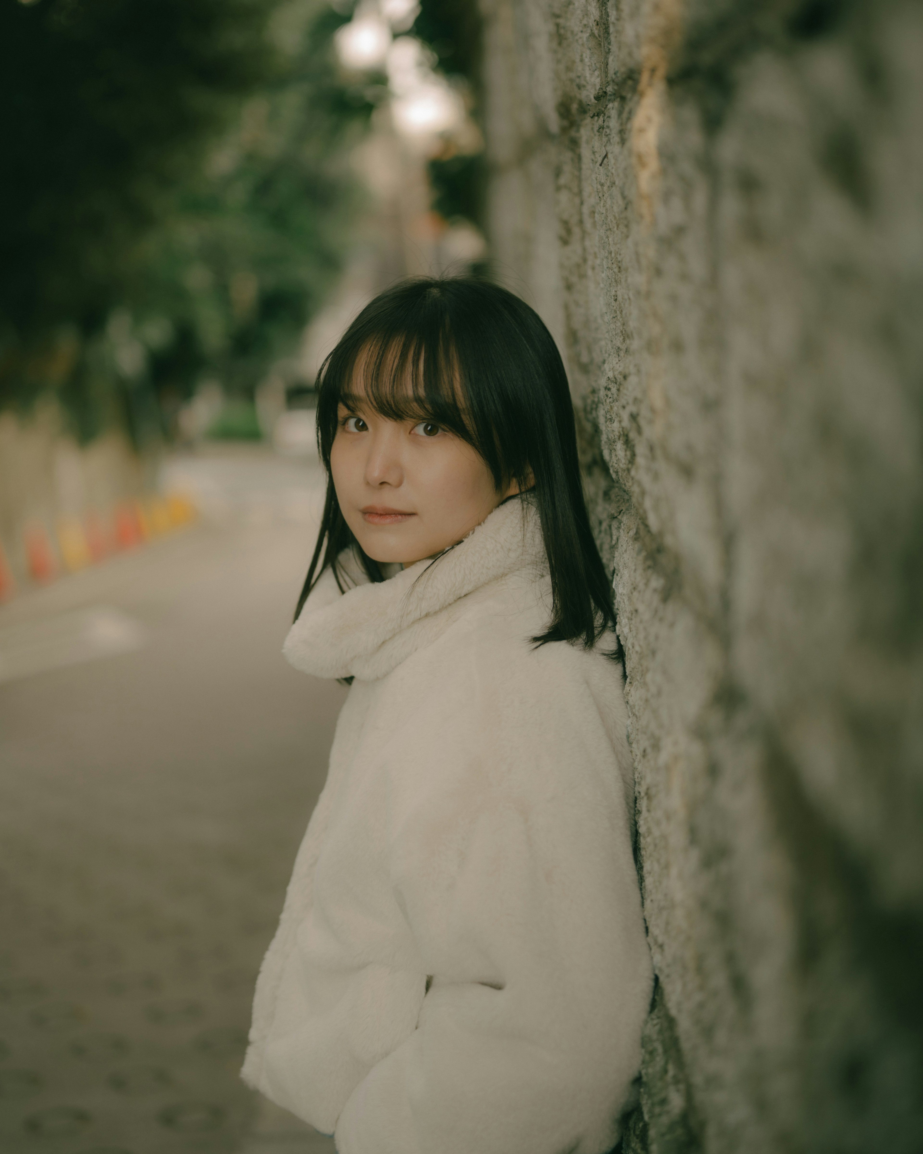 Una donna in un cappotto bianco appoggiata a un muro di pietra