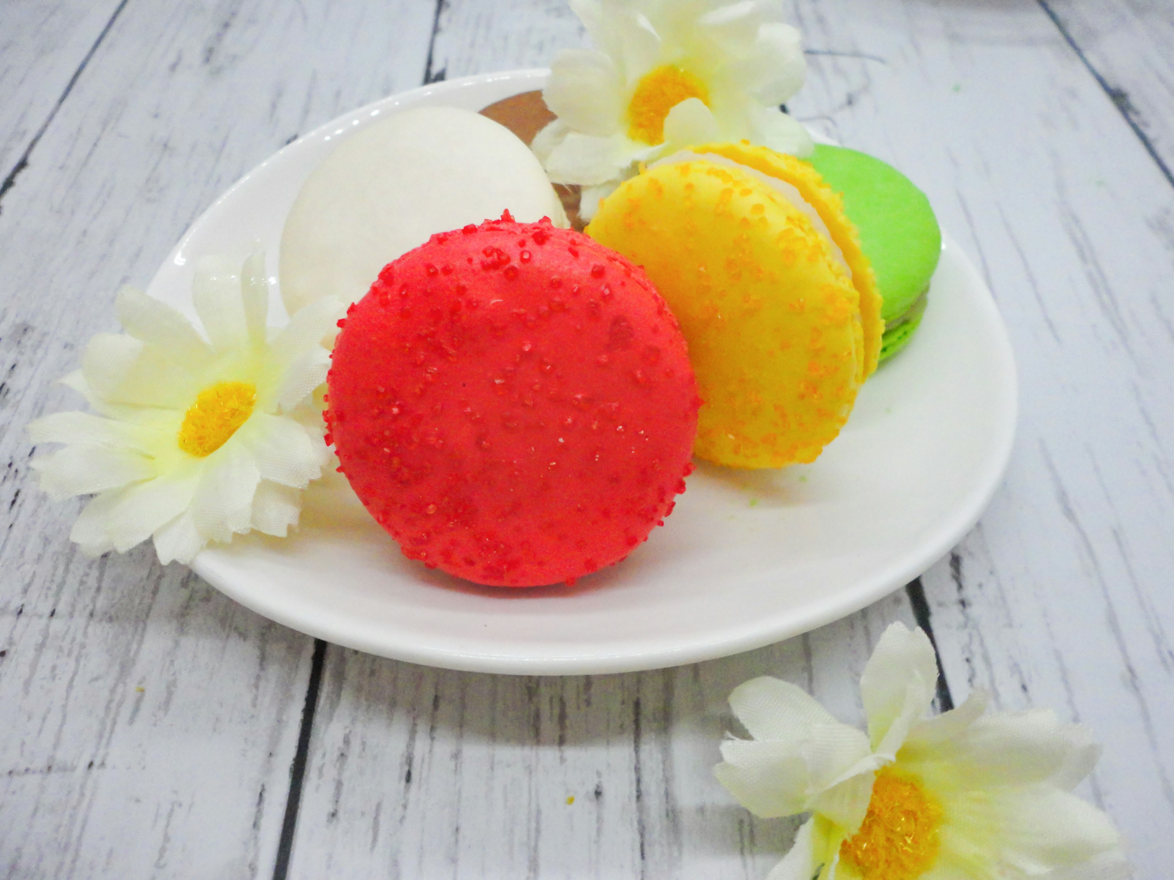 Bunte Macarons mit weißen Blumen auf einem Teller angeordnet