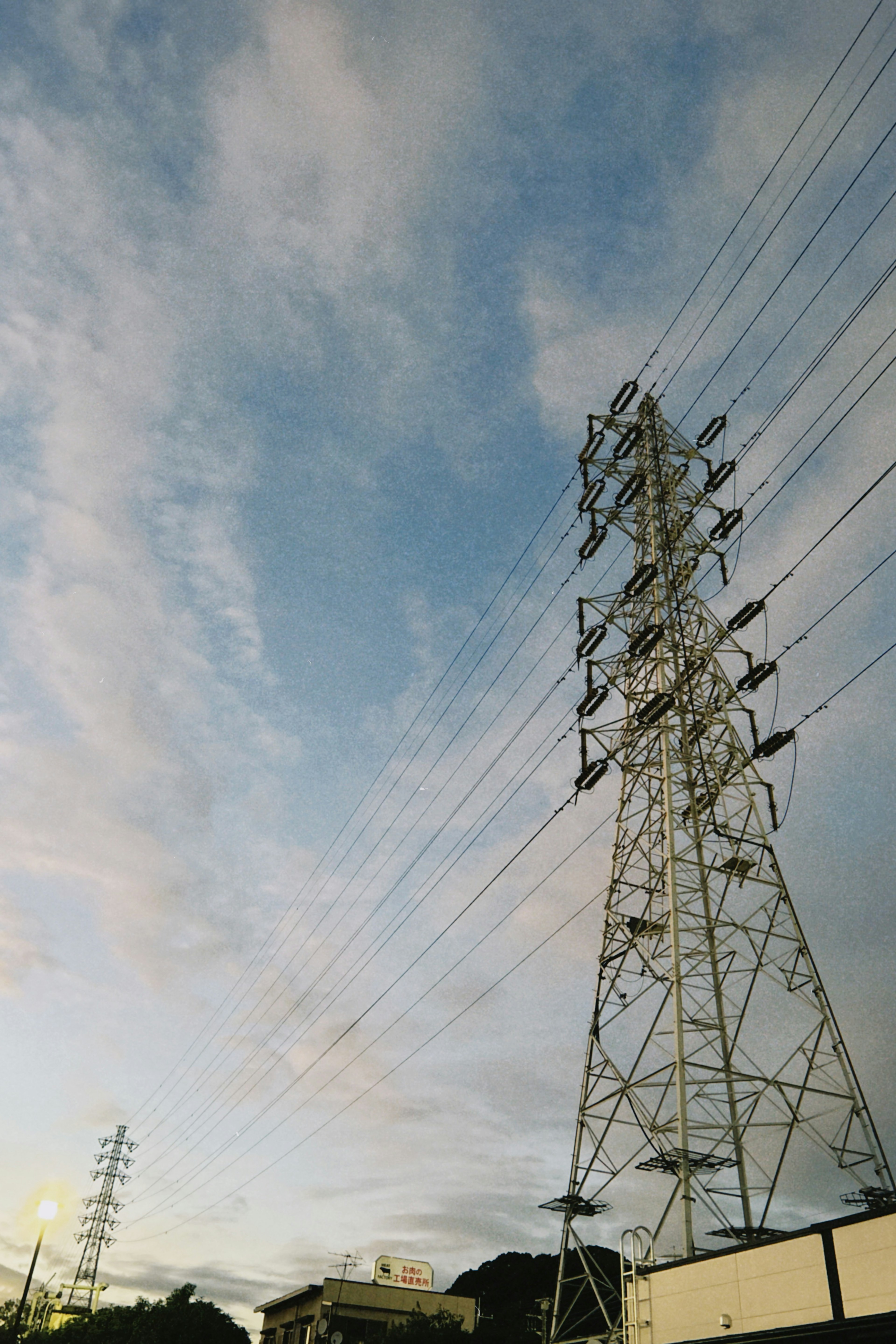 Menara listrik tinggi di bawah langit biru dan awan