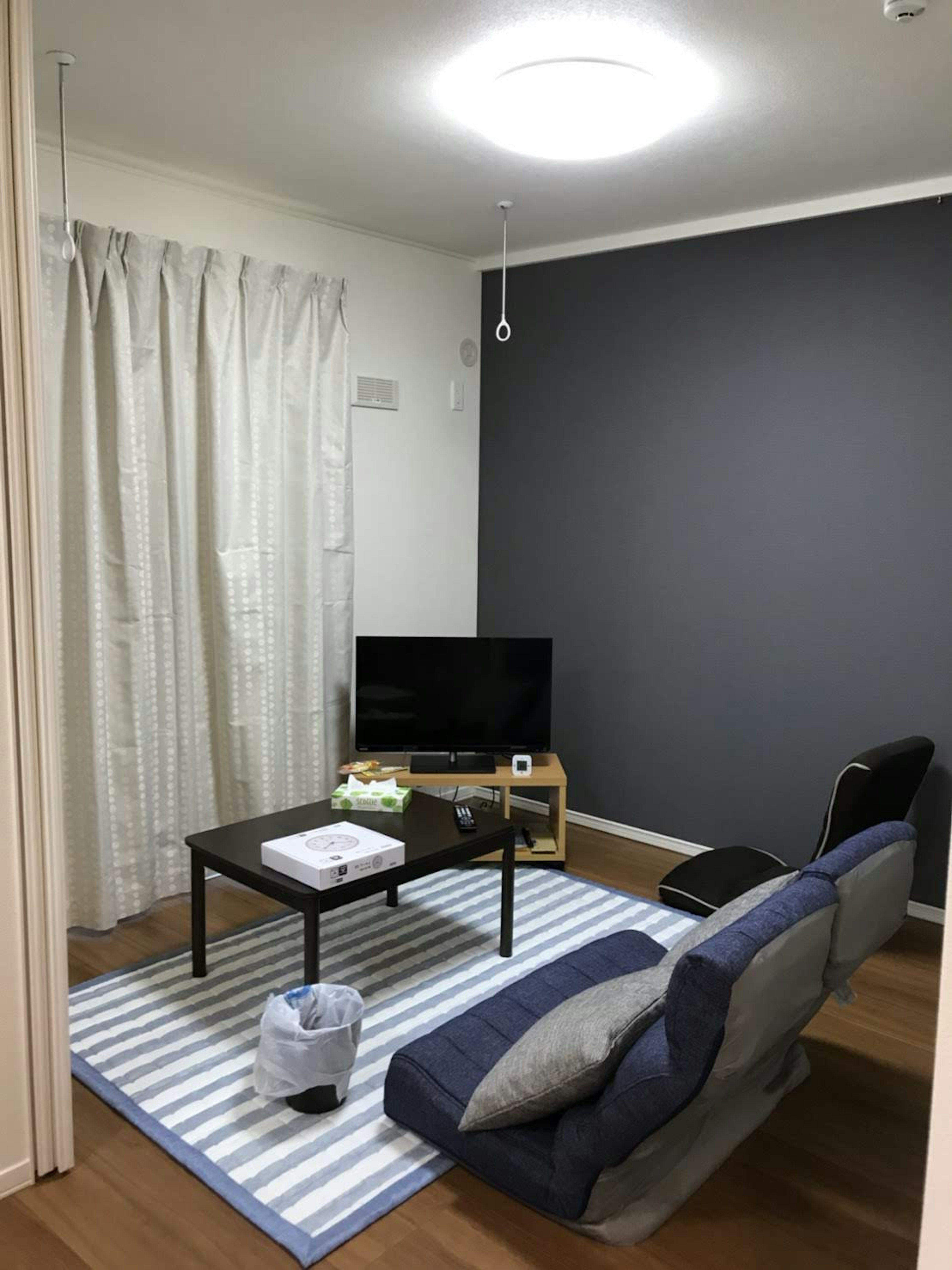 Sala de estar acogedora con sofá azul y mesa negra, televisión y cortinas