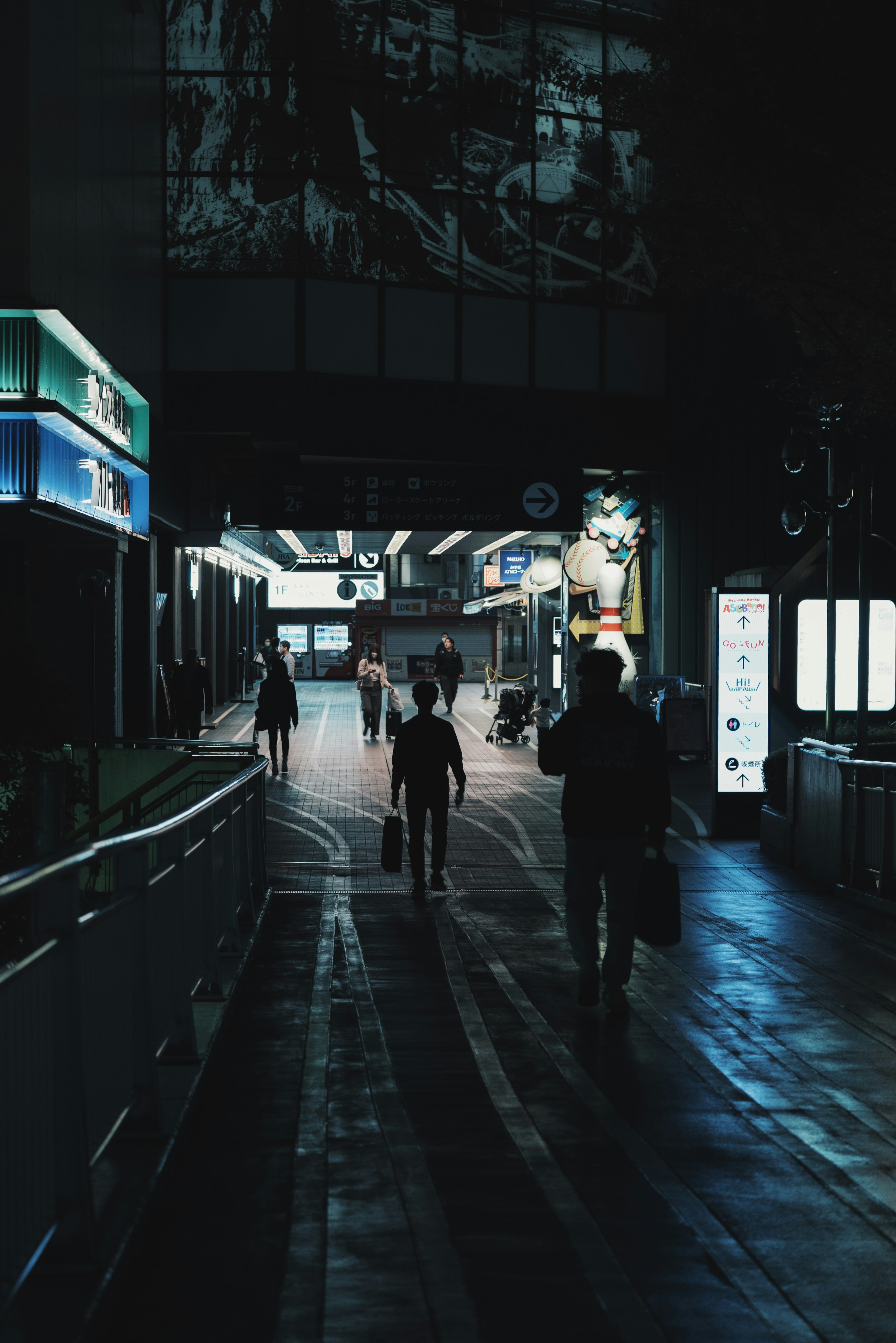 People walking in a dark corridor with blue lighting at a station