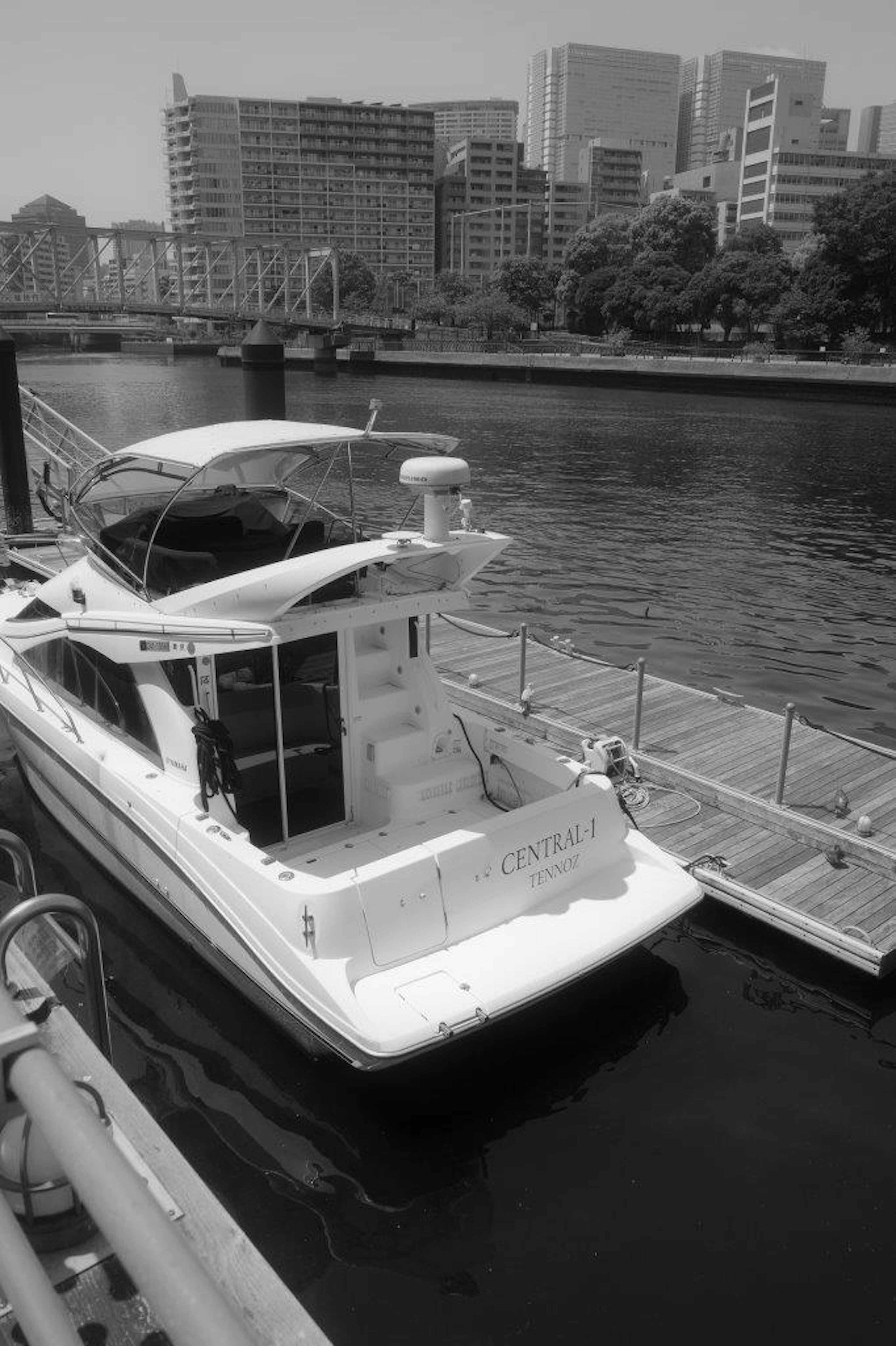 Black and white image of a boat docked by the water with skyscrapers in the background