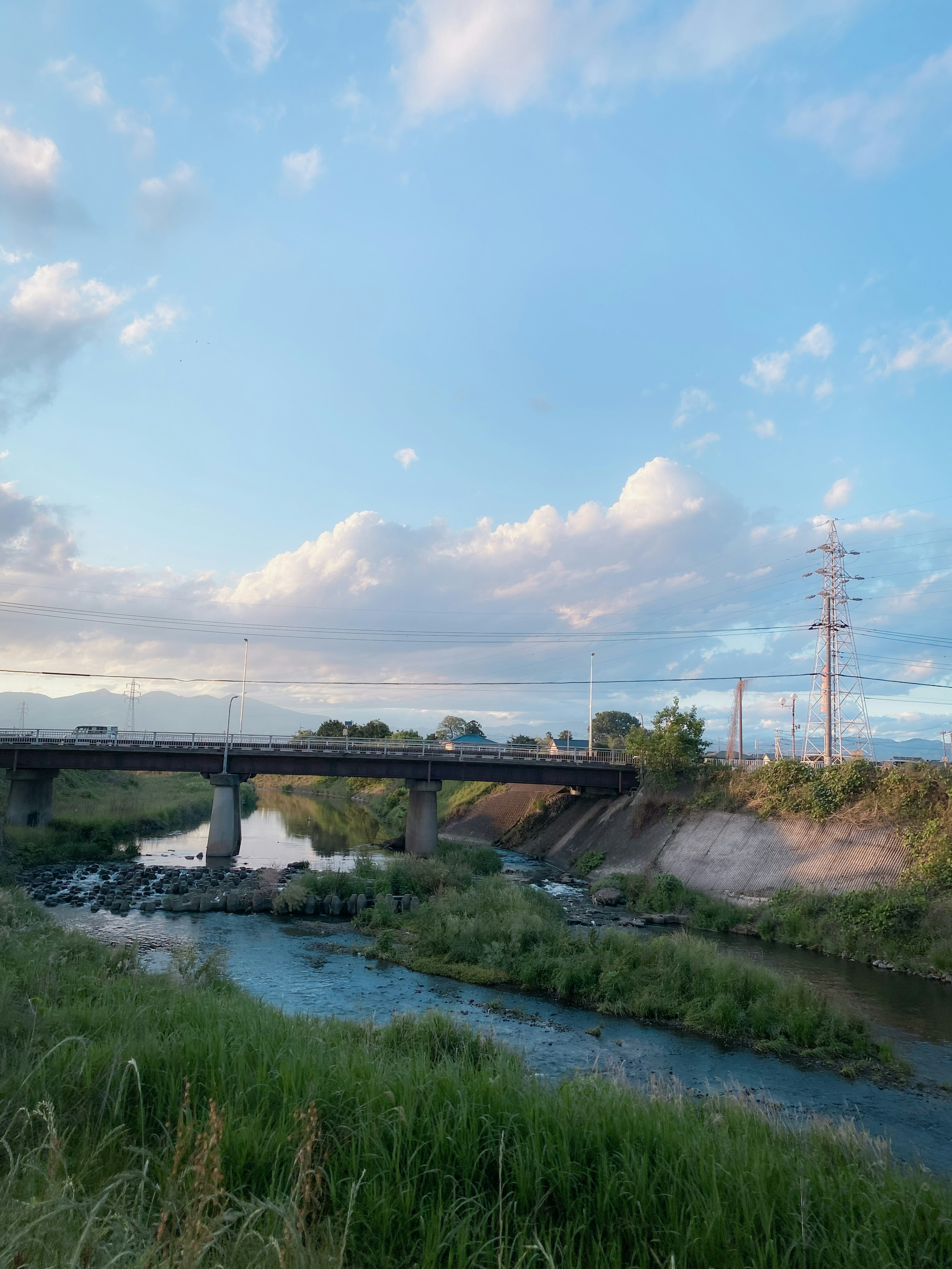 青空の下に広がる草原と川が流れる風景 橋と電柱が見える