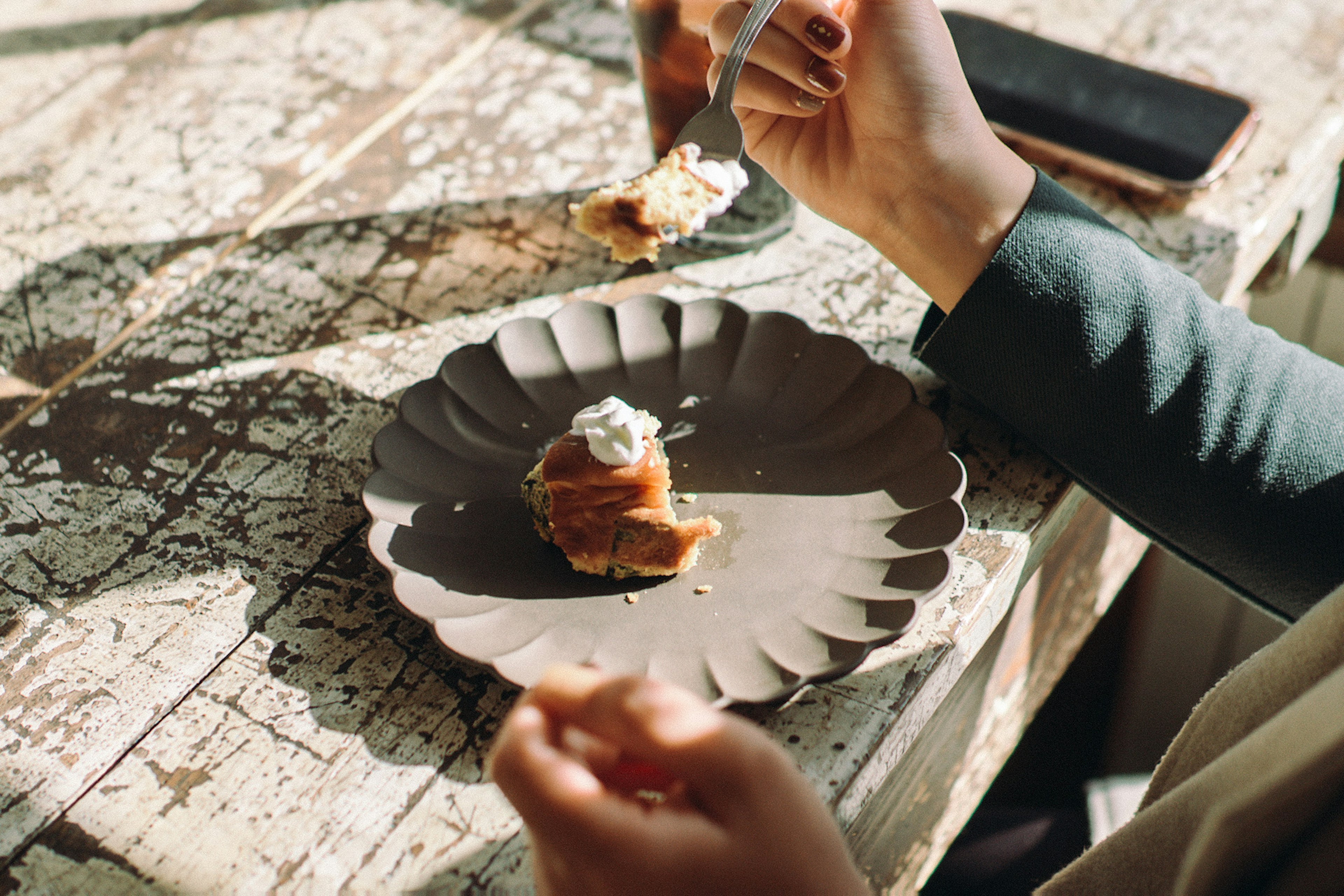 Person holding a spoon enjoying dessert on a black plate