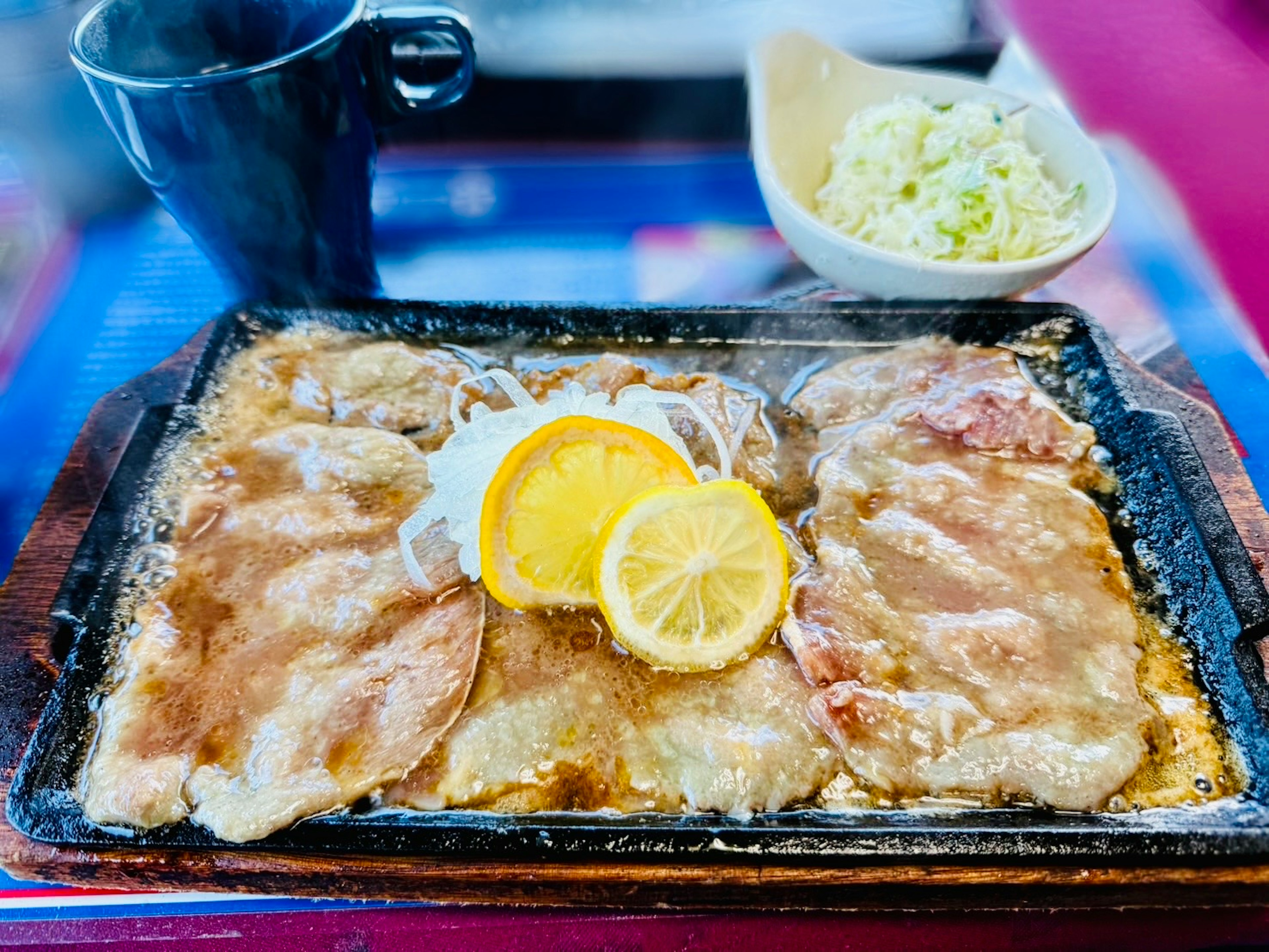 Sizzling pork dish on a hot plate with lemon slices