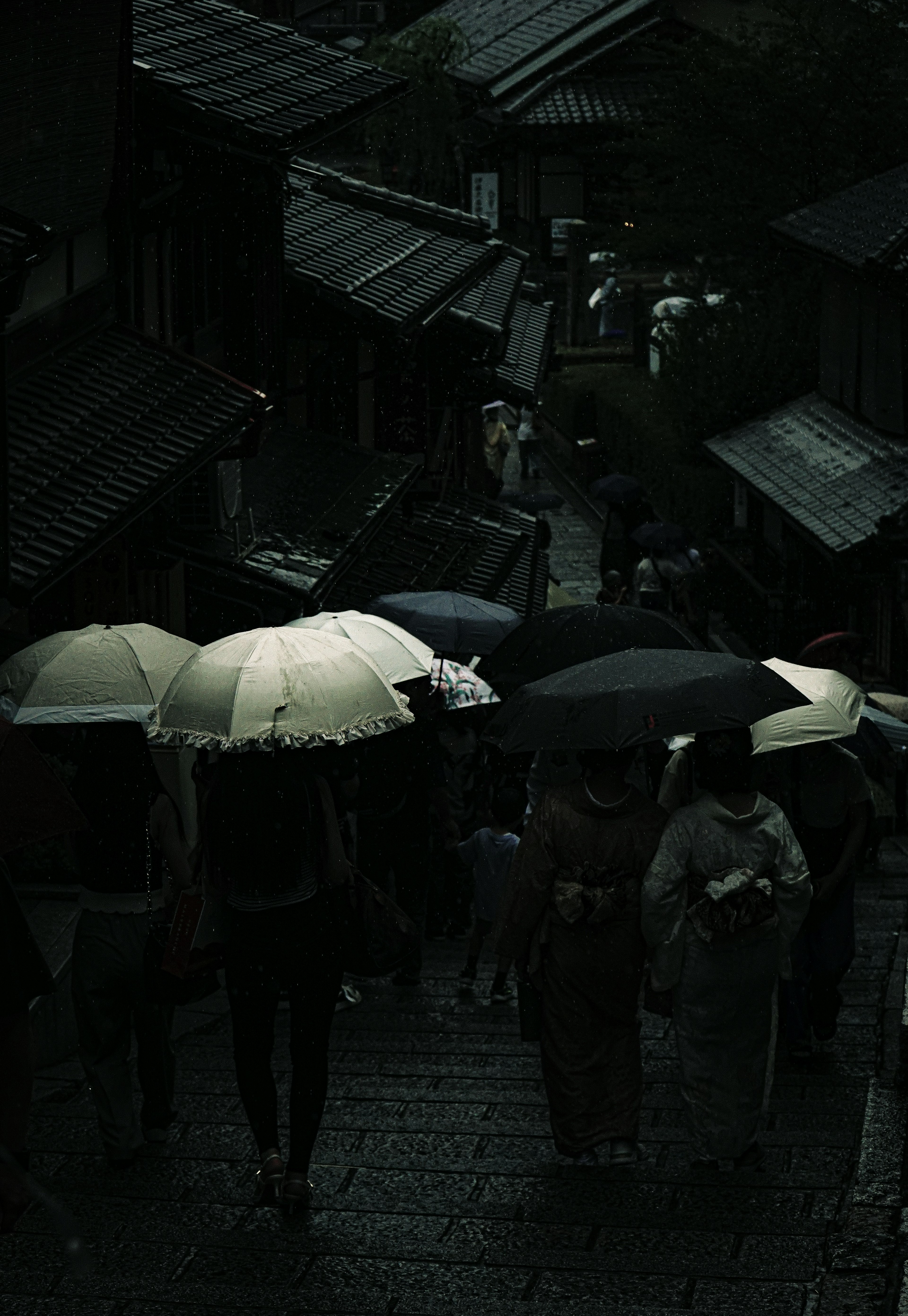 Des gens marchant sous la pluie avec des parapluies dans une rue étroite