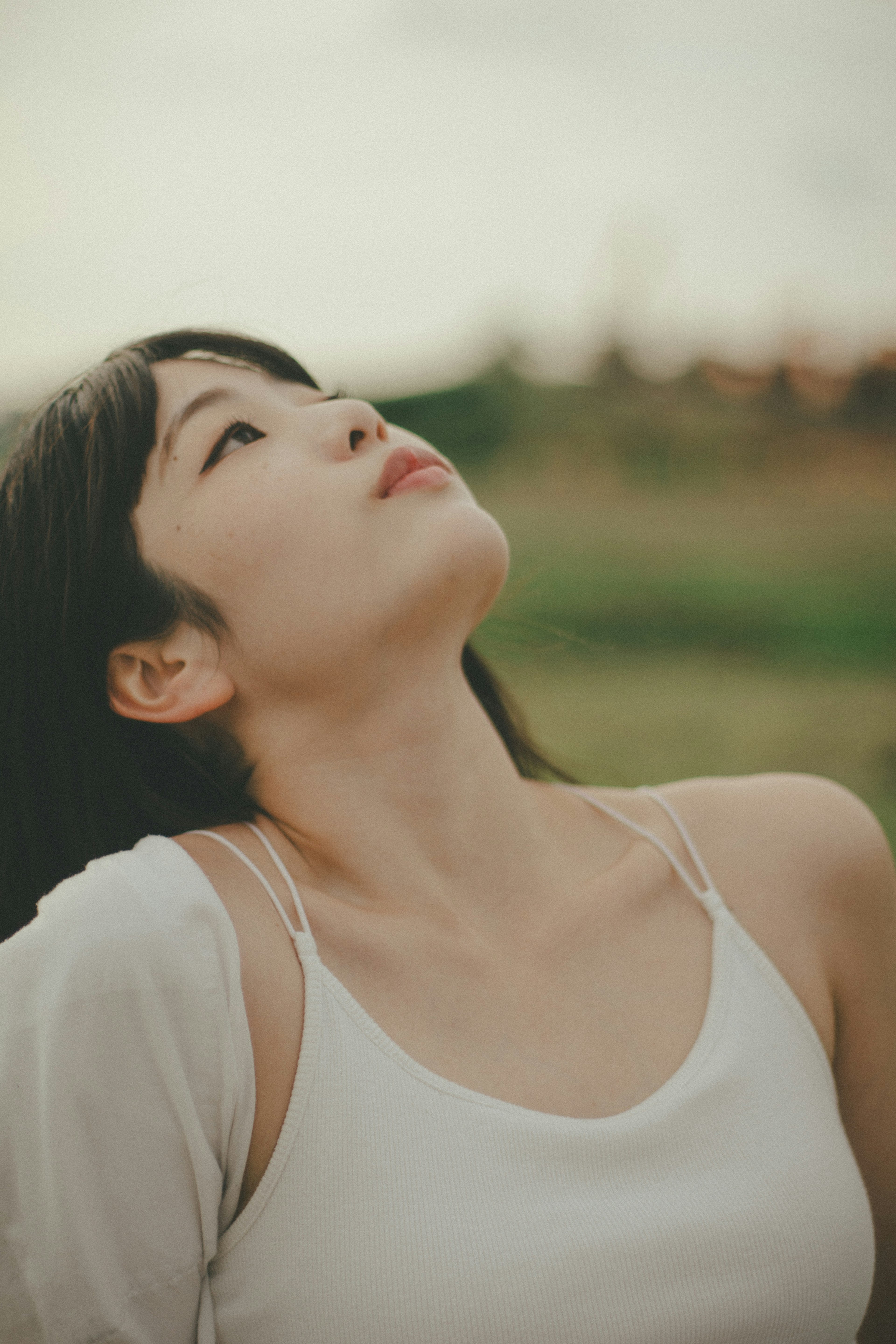 若い女性が空を見上げているシーン背景には緑の草原が広がっている