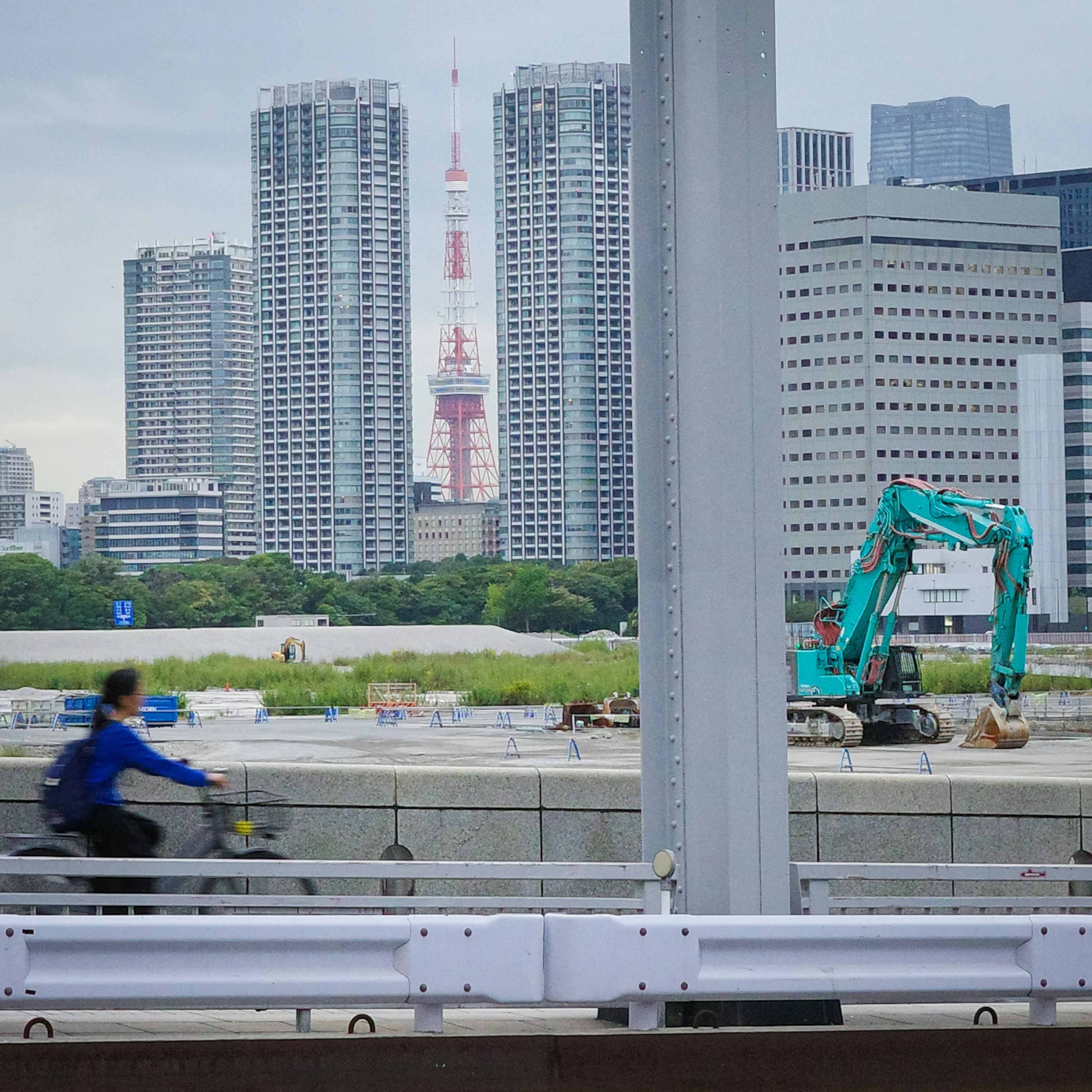 Seorang pesepeda di jembatan dengan Menara Tokyo di latar belakang dan peralatan konstruksi di dekatnya