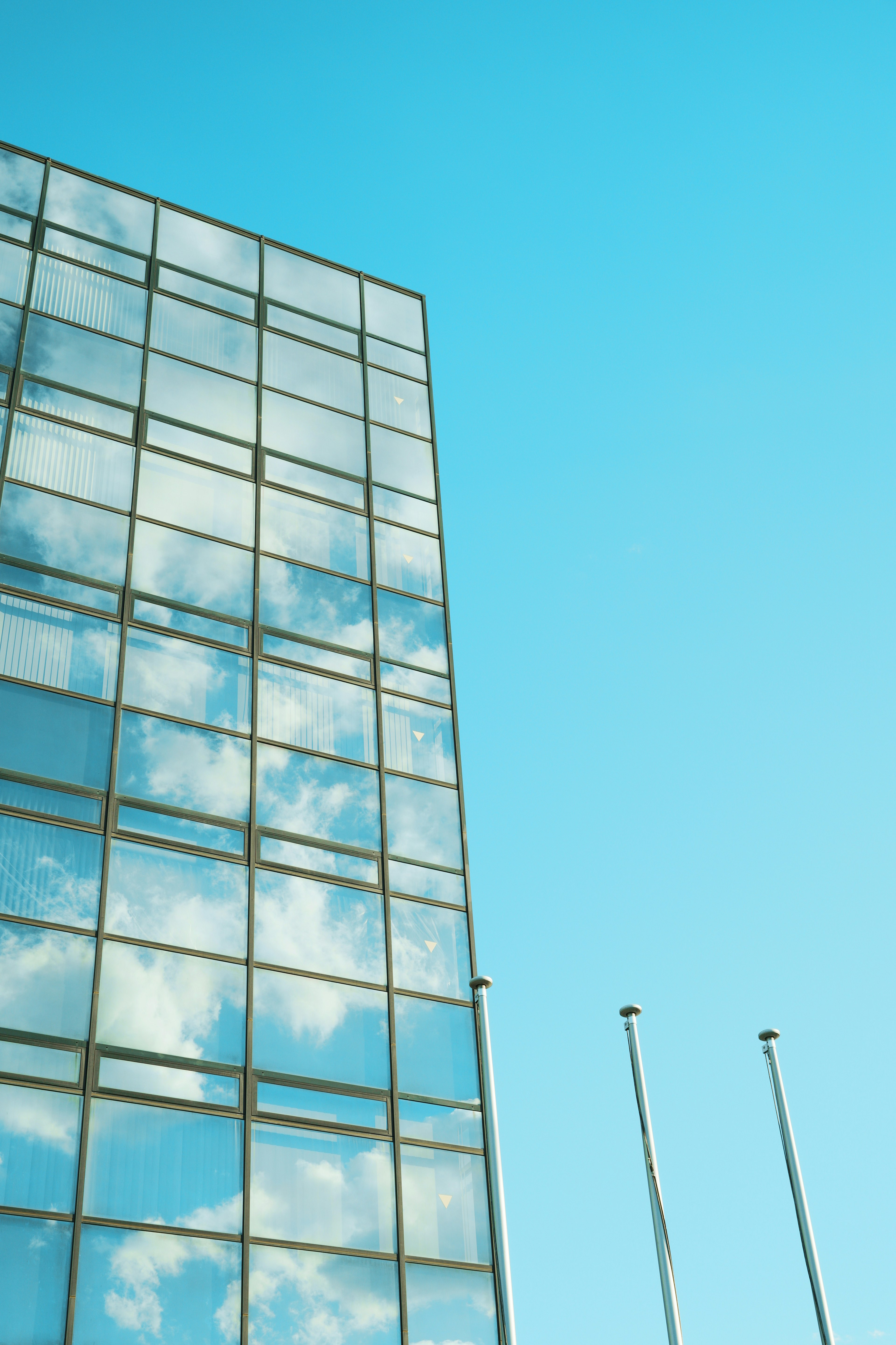 Parte di un edificio in vetro che riflette il cielo blu e le nuvole con pali della bandiera