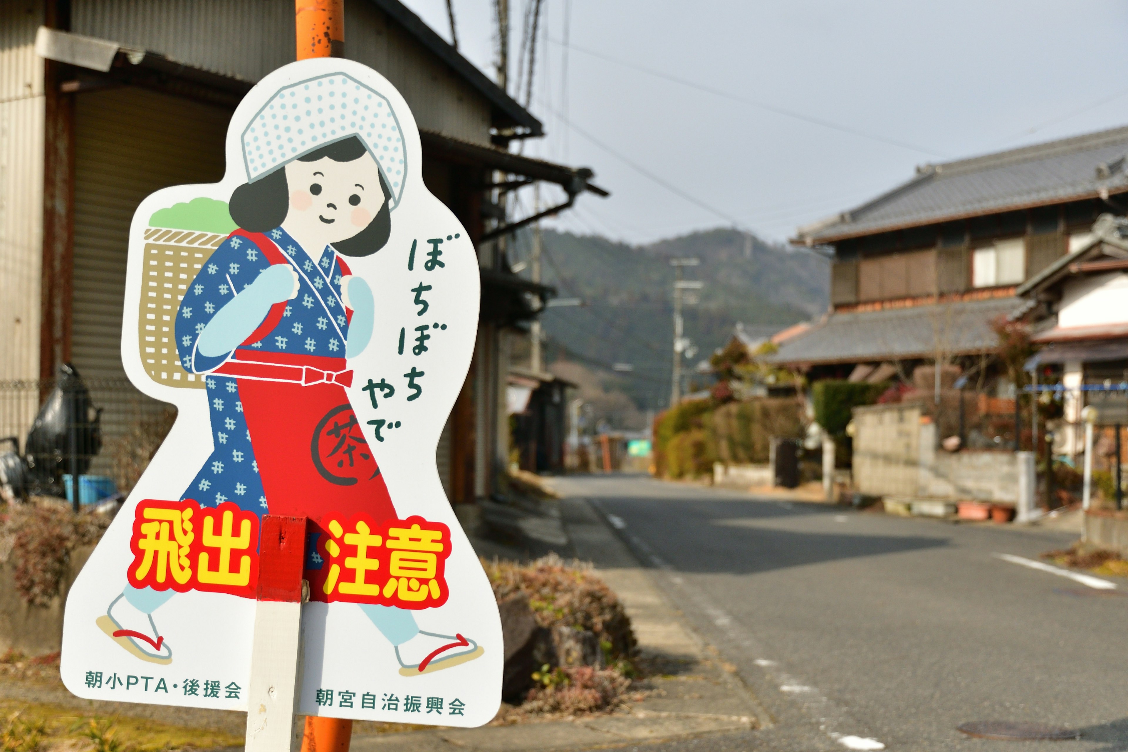 家屋と道路が見える風景に立つ飛び出し注意の看板女の子のイラスト