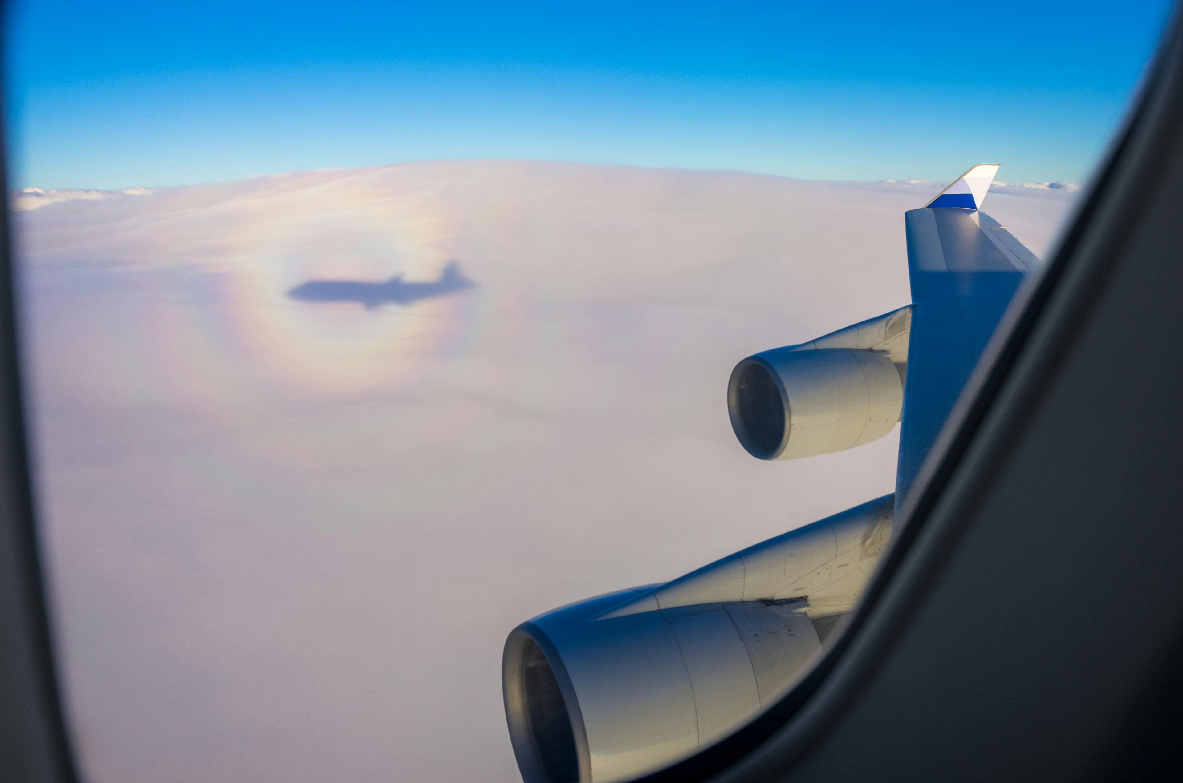 View of airplane wing and engine above the clouds airplane shadow visible in the clouds