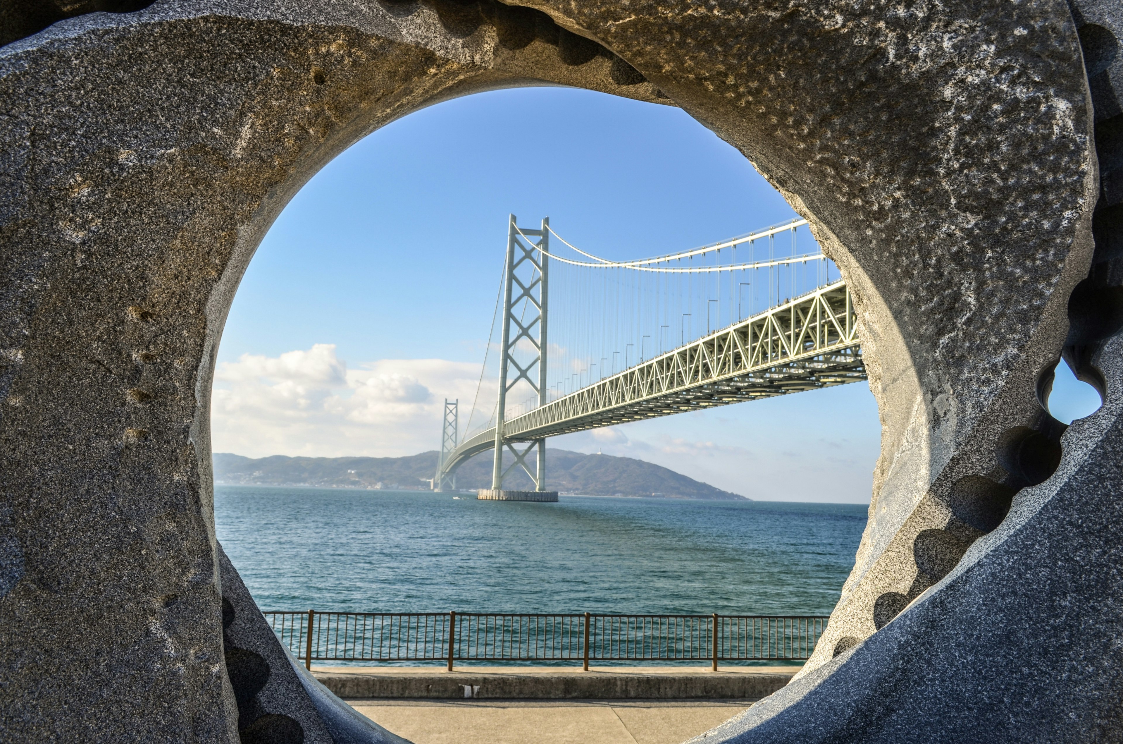 Scenic view of a bridge through a circular stone frame by the sea