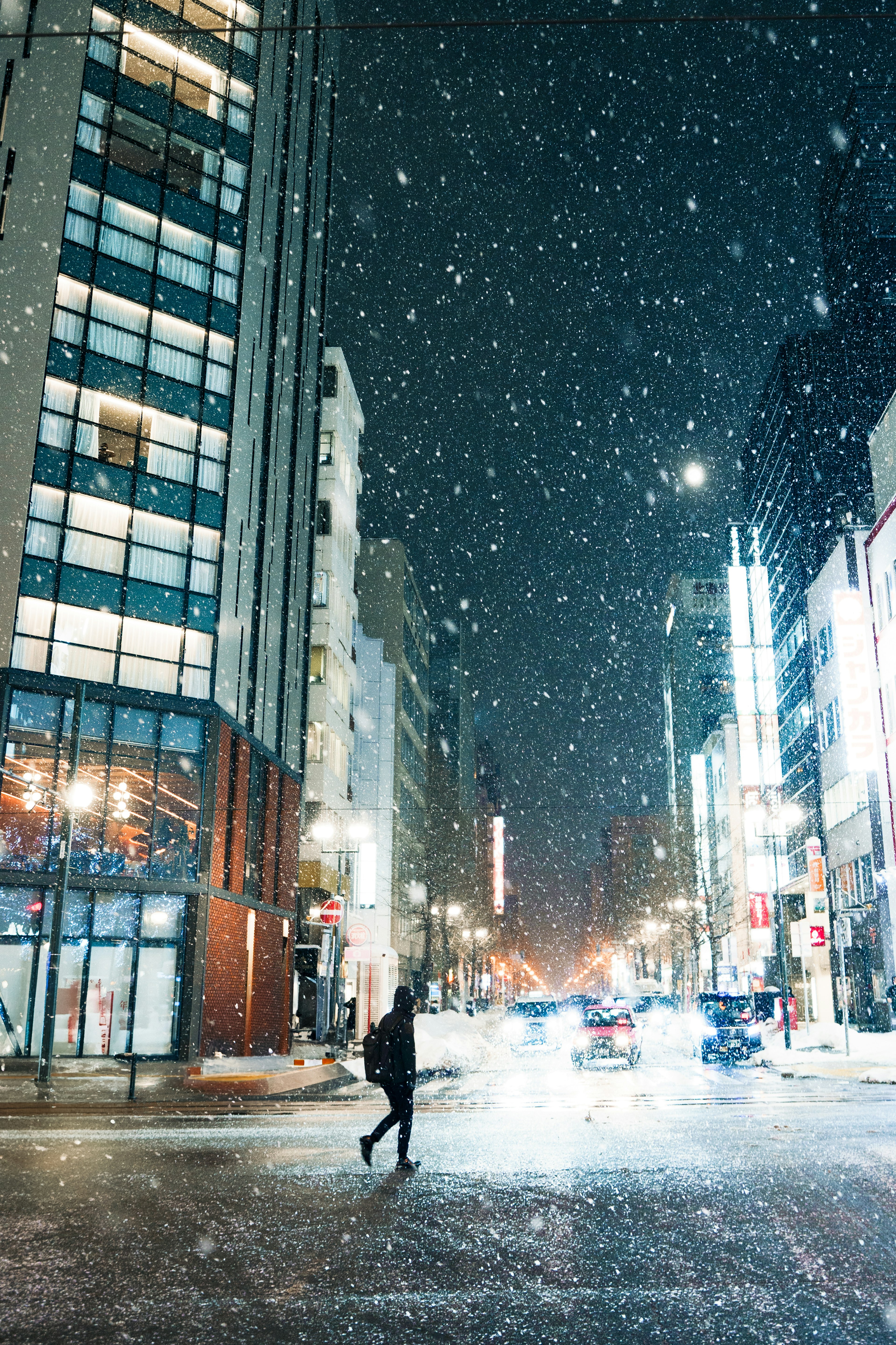 Person crossing a snowy street at night with buildings in the background