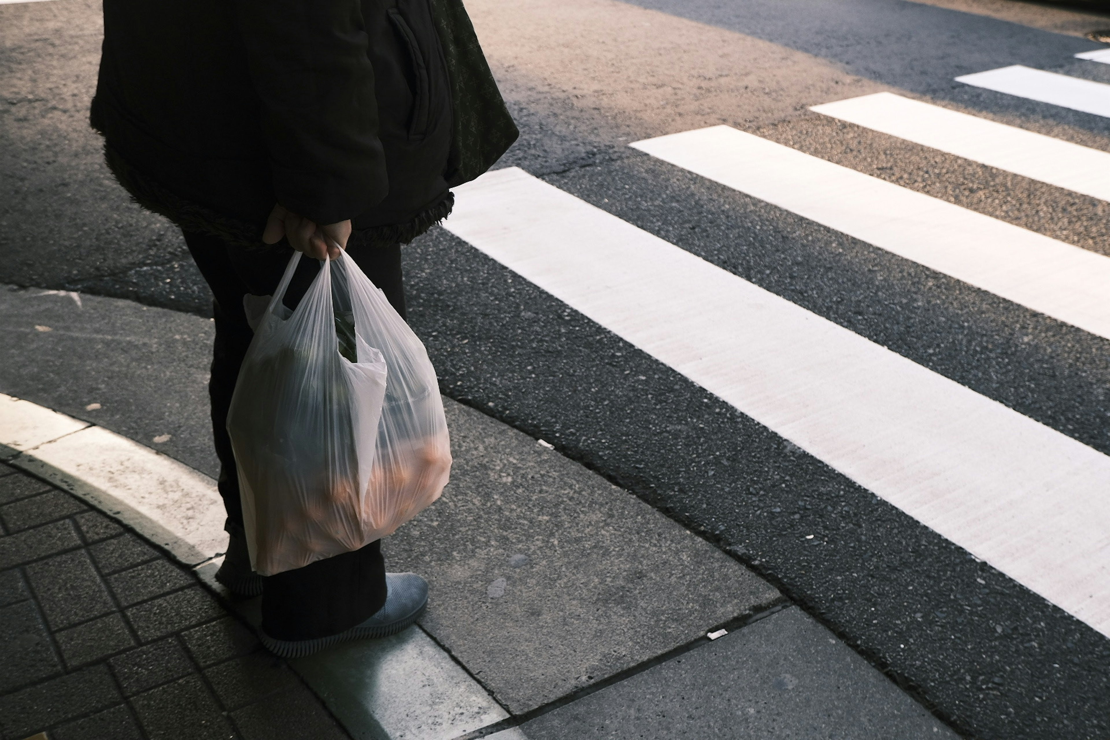 Person standing at crosswalk holding shopping bag