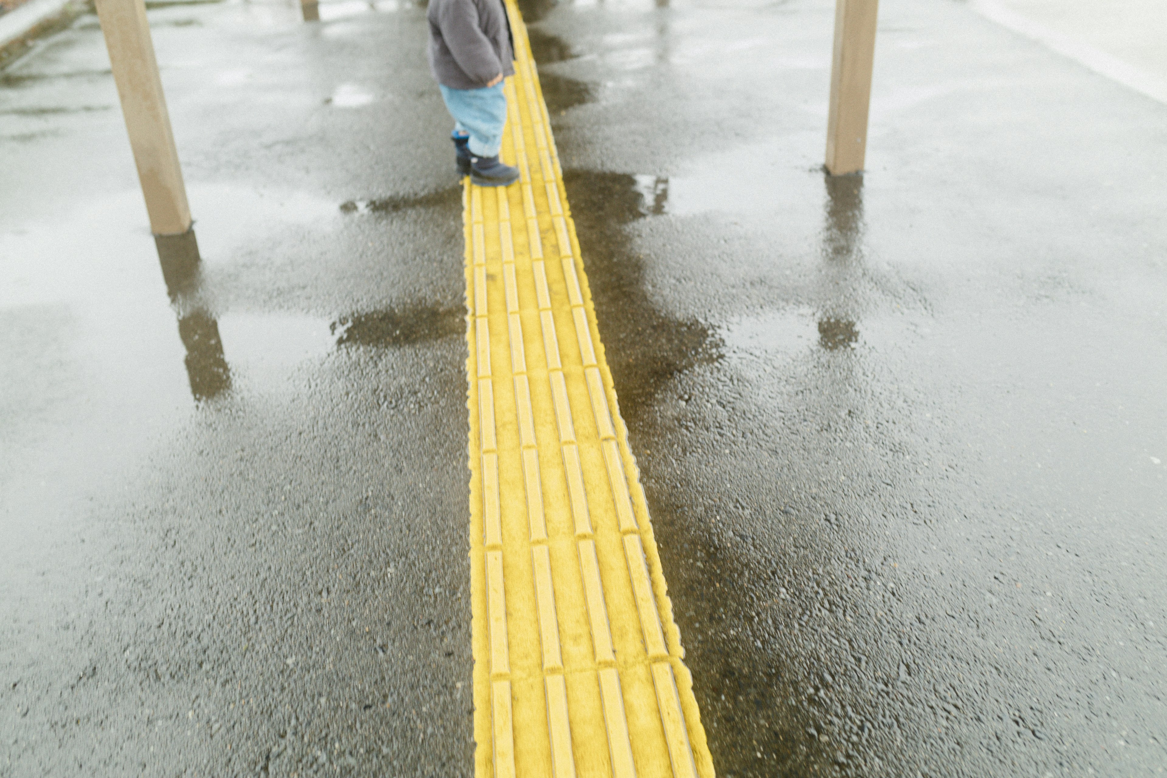 A pedestrian walking on a yellow tactile paving strip on wet asphalt