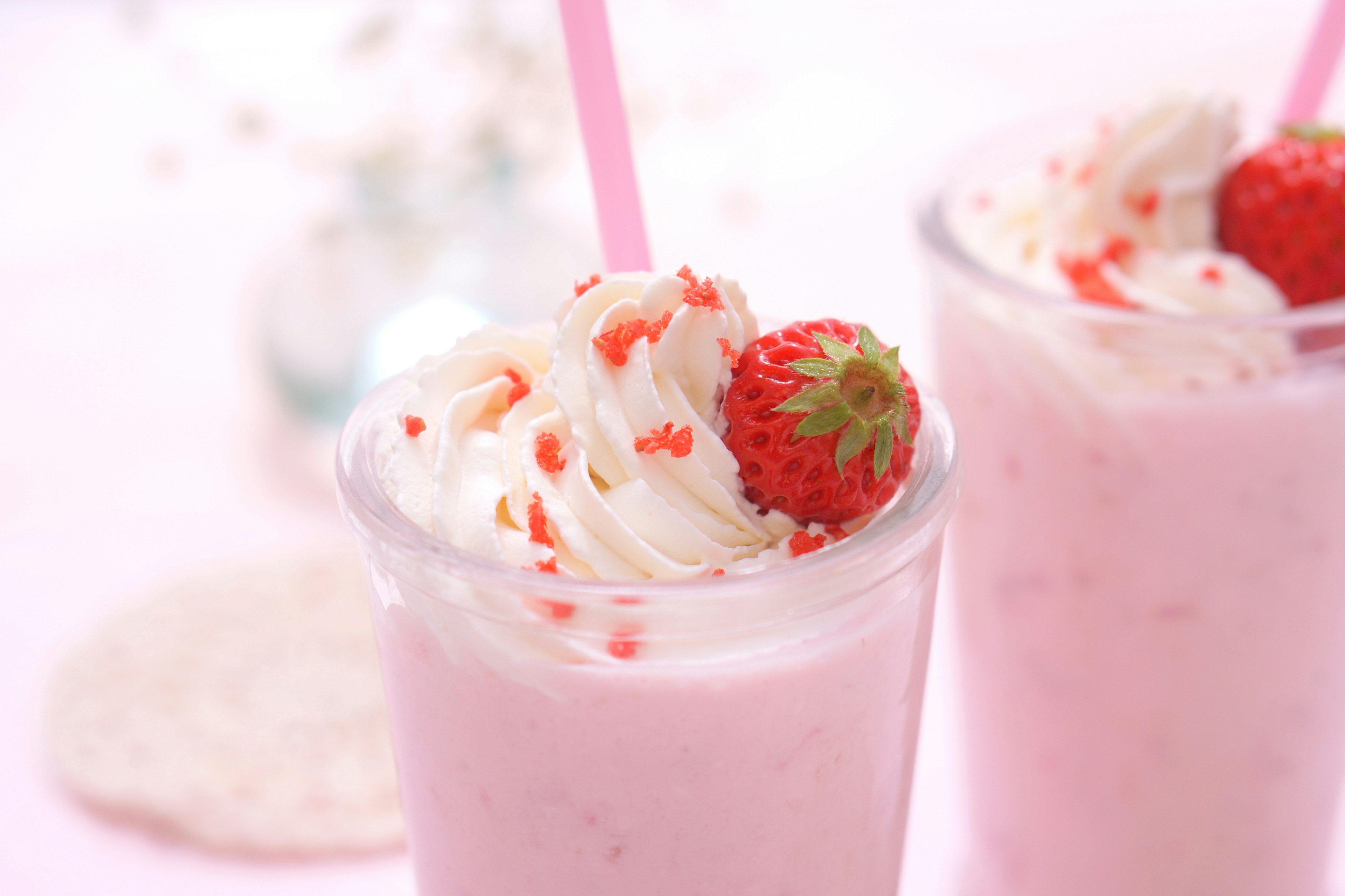 Creamy strawberry shake topped with whipped cream and strawberries against a beautiful pink background