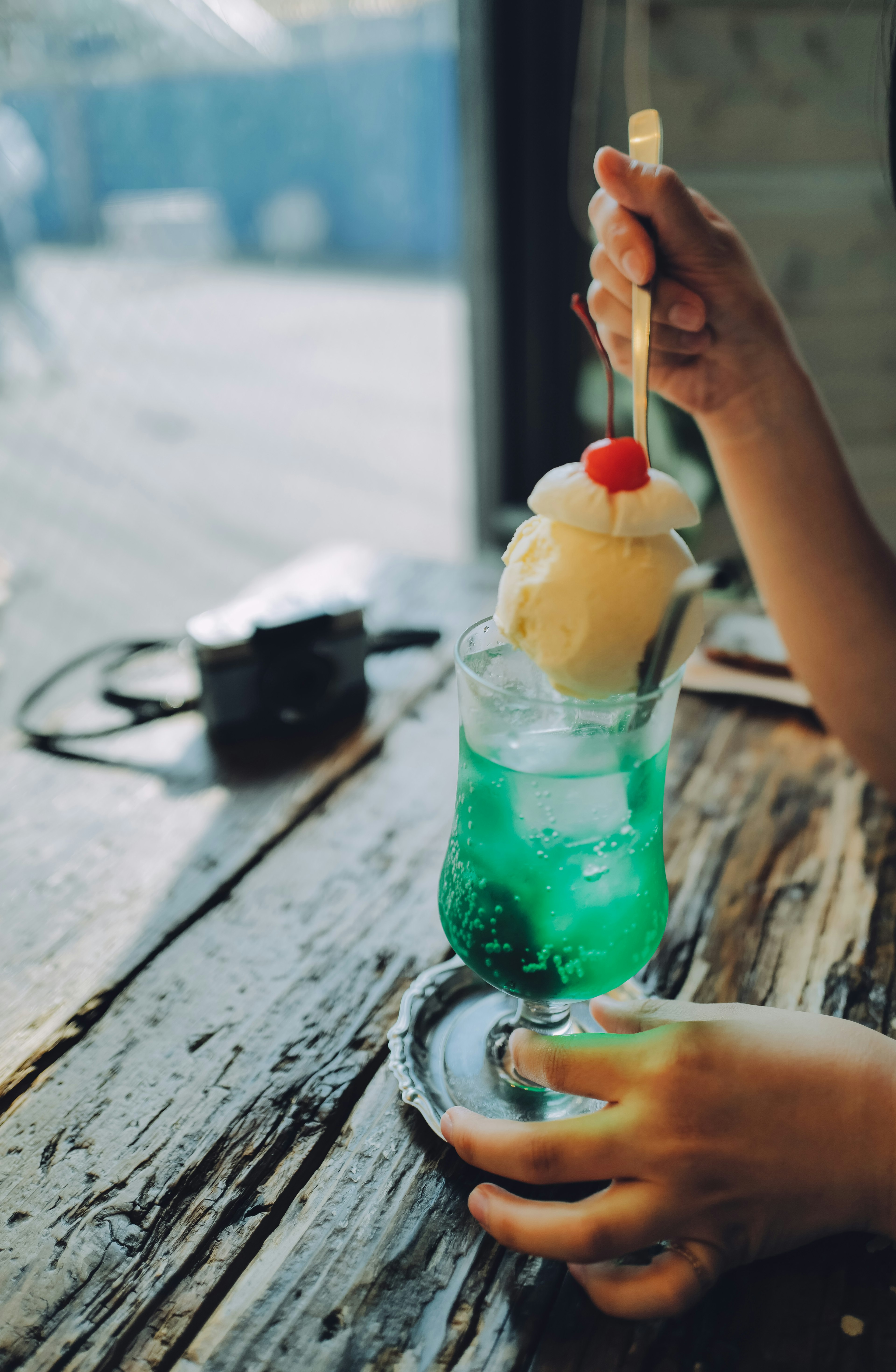 Eine Hand hält einen Dessert-Cocktail mit blauer Flüssigkeit, bedeckt mit Eiscreme und Kirsche