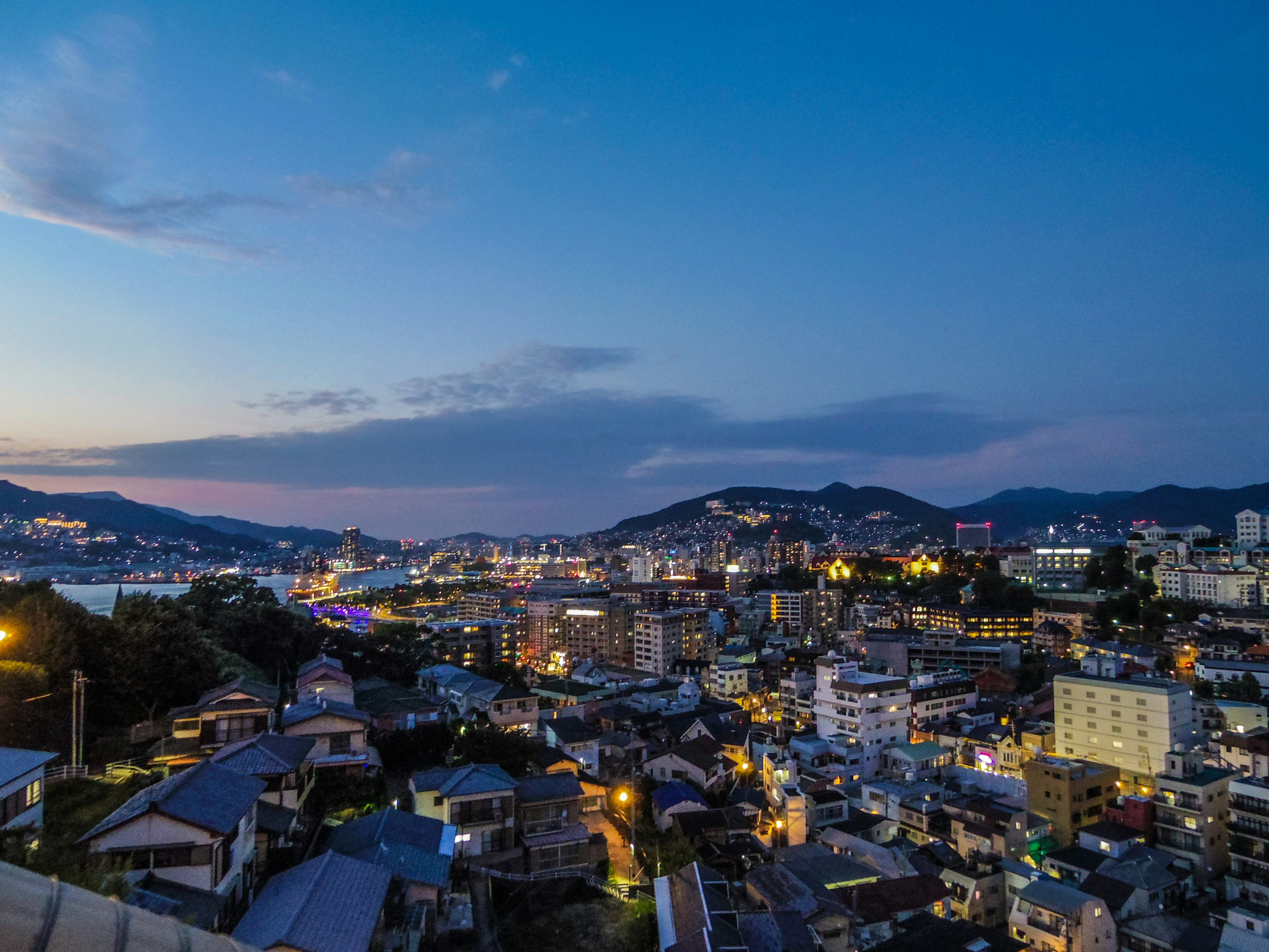 Vista nocturna de una ciudad con edificios y montañas al fondo