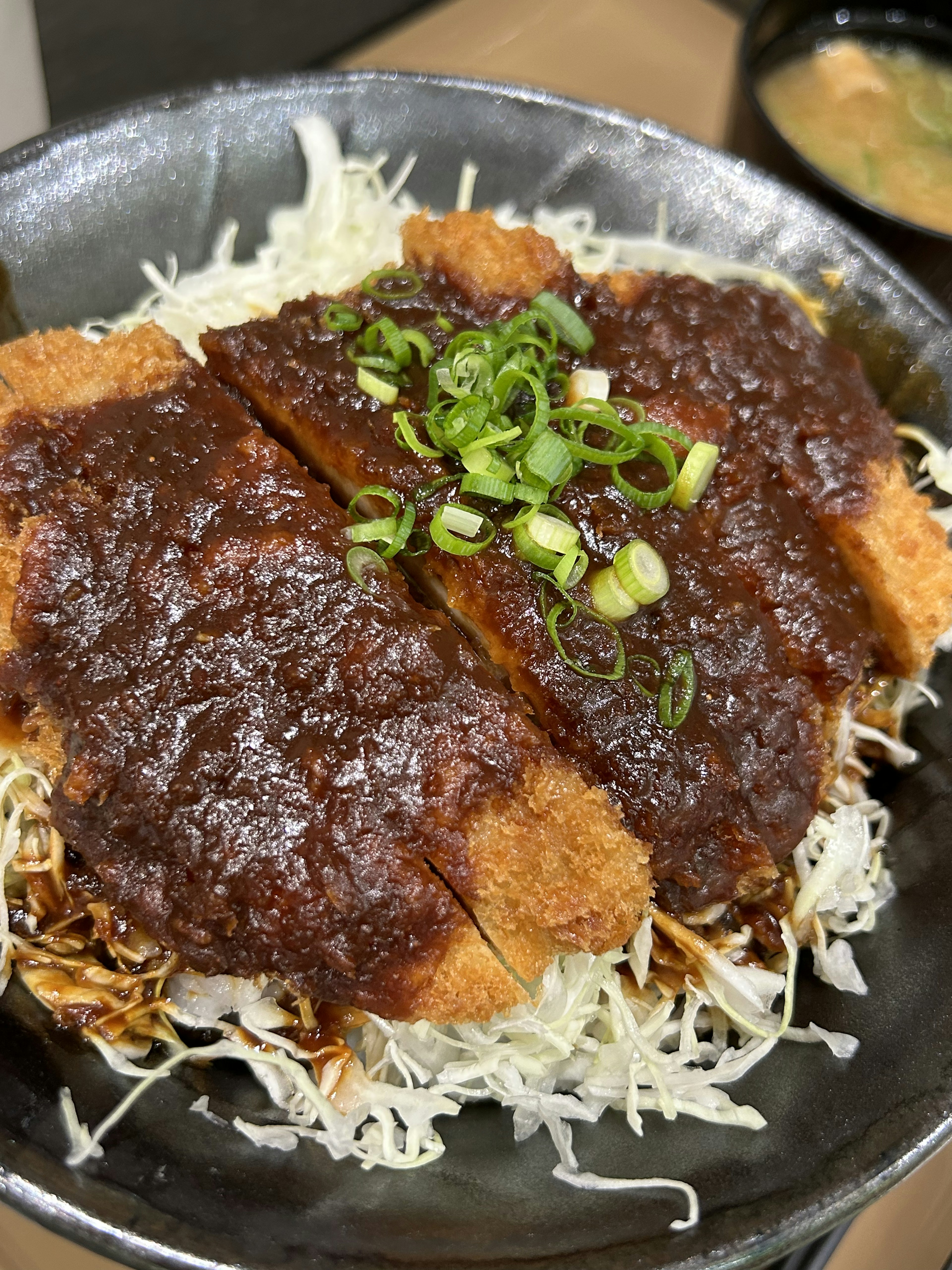 Piatto con cotoletta di maiale guarnita con salsa dolce e saporita e cipollotti