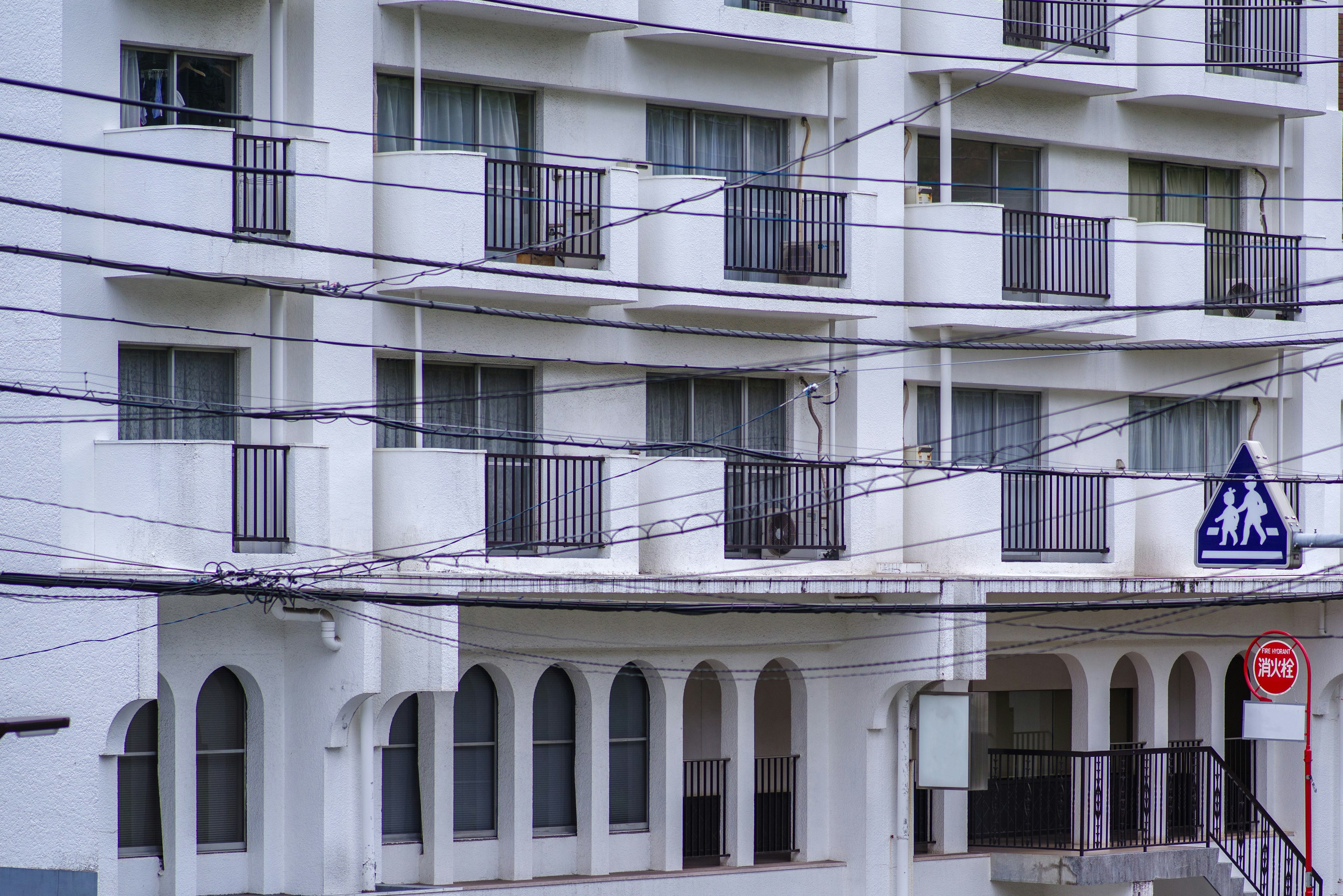 Tampilan sebagian dari gedung apartemen putih dengan balkon dan kabel listrik