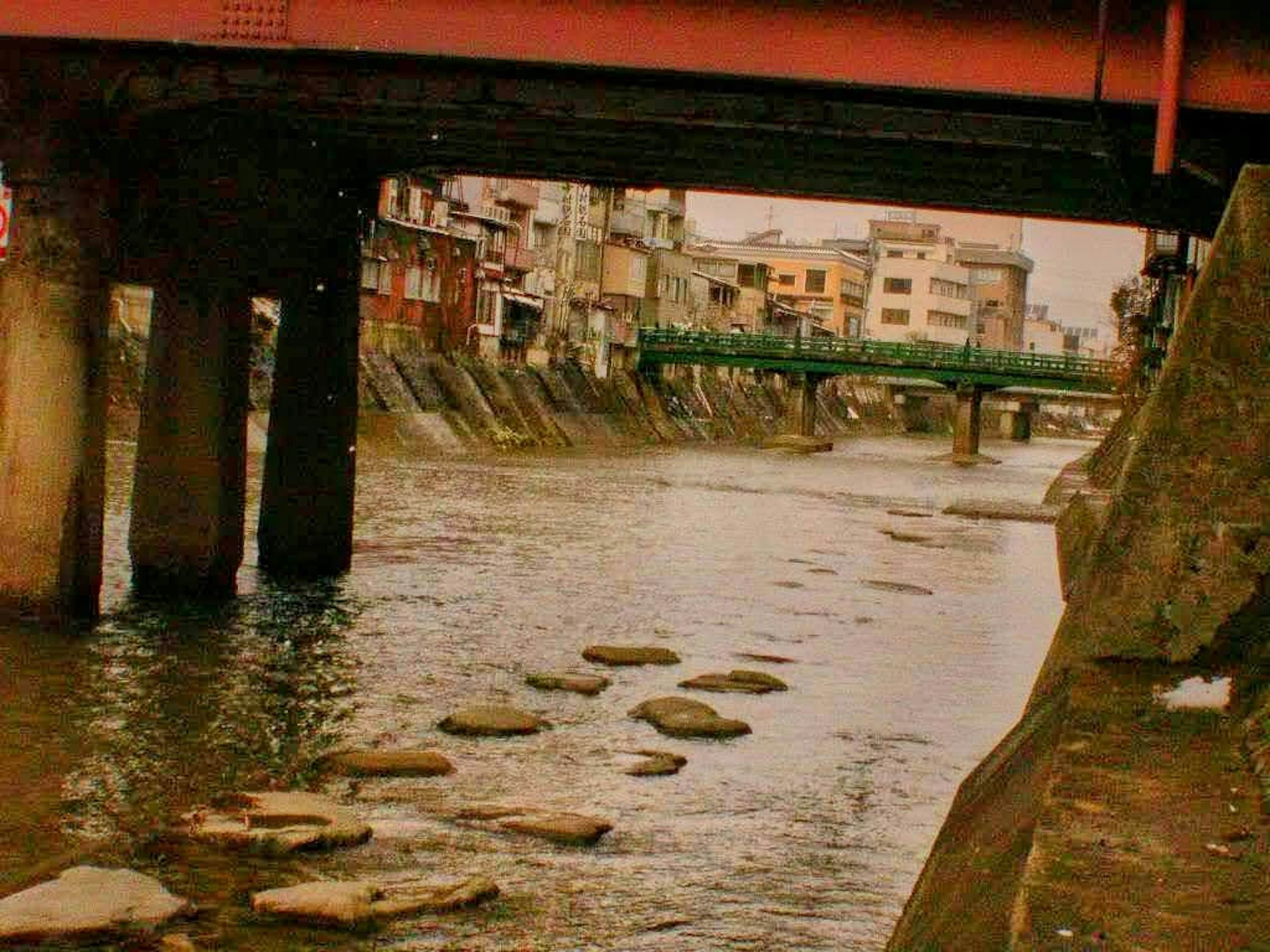 Bridge pillars over a river with stepping stones visible