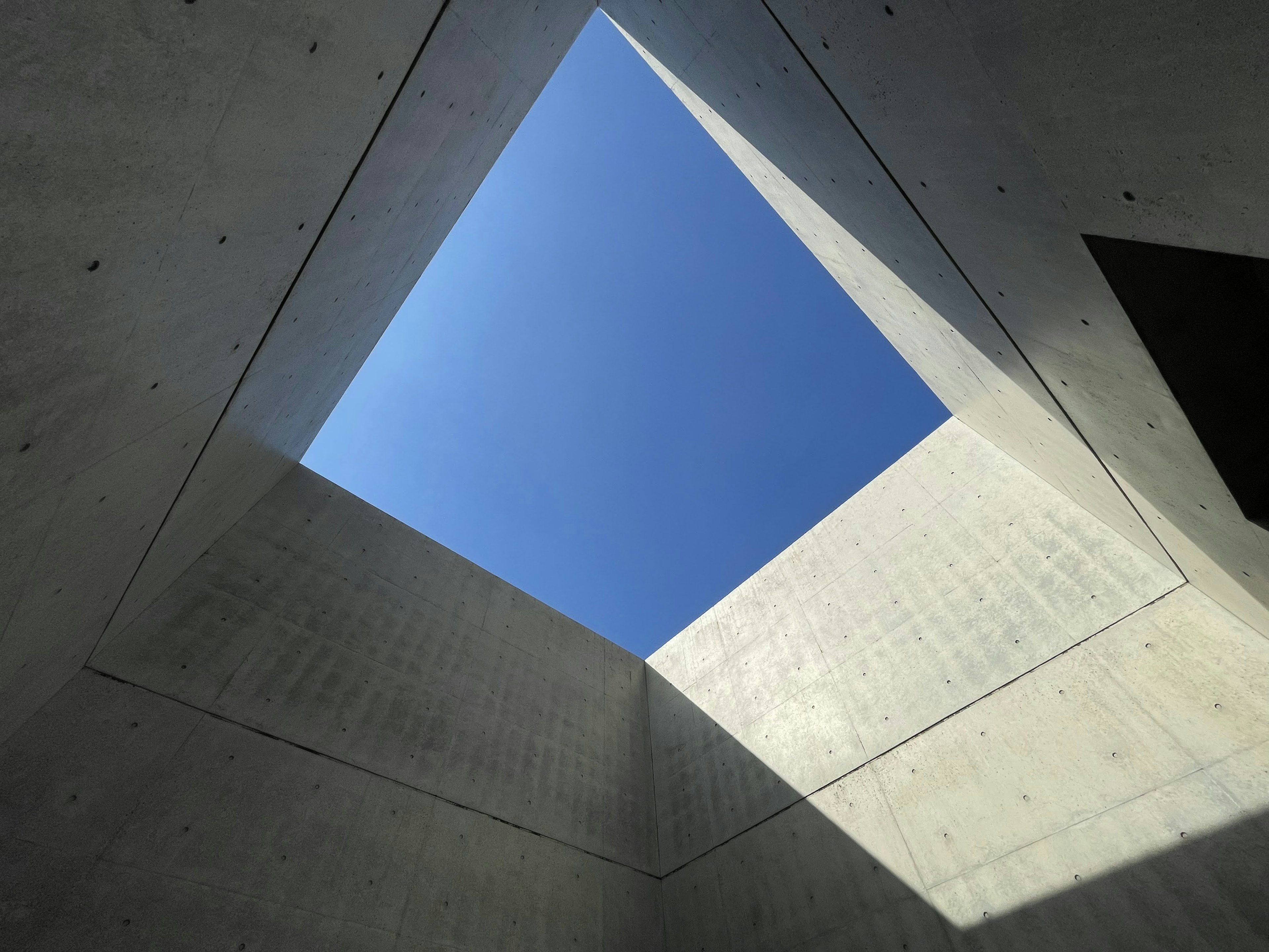 Ouverture carrée révélant le ciel bleu d'une structure en béton