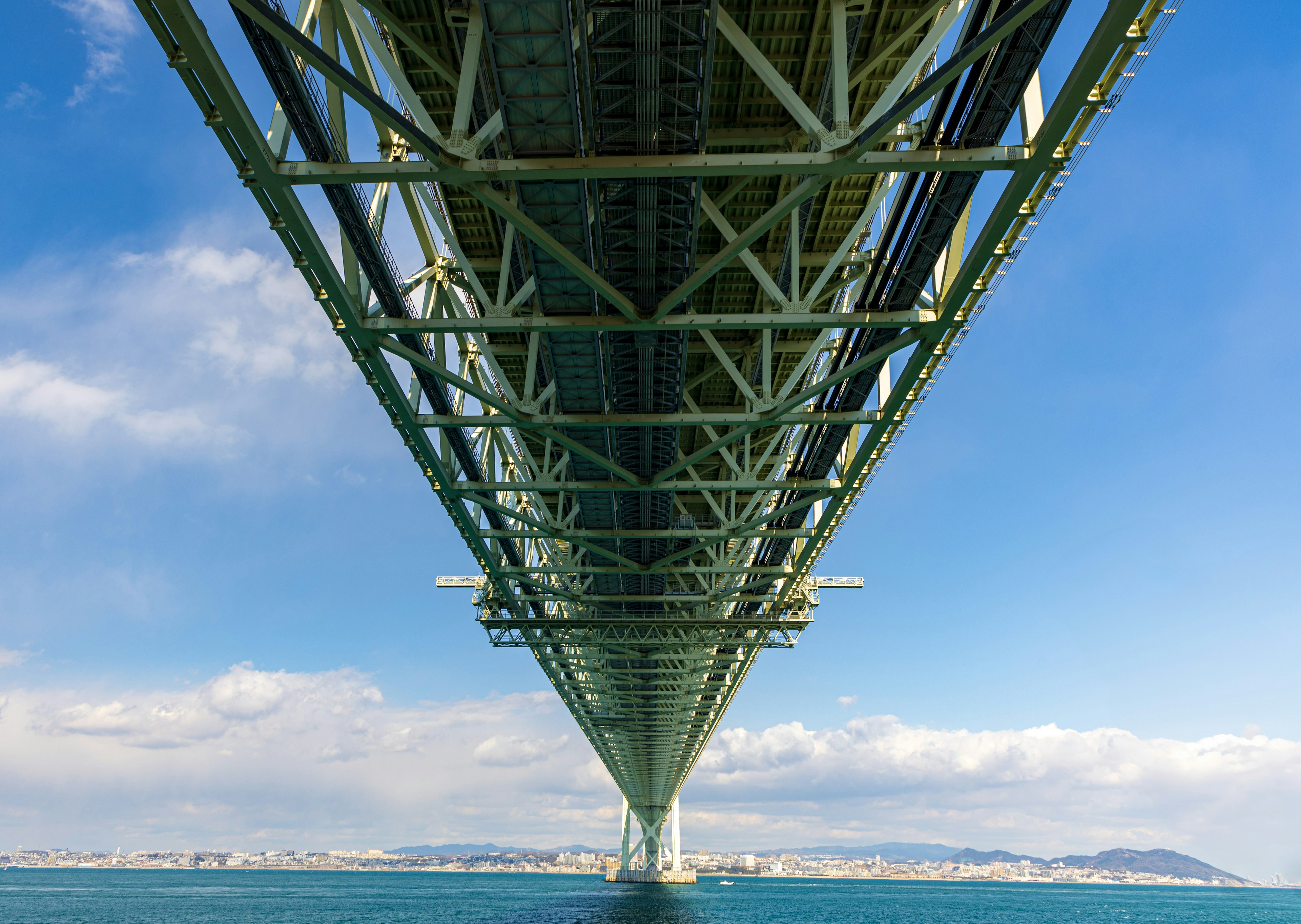 Vista de una estructura de puente desde abajo con cielo azul y nubes al fondo