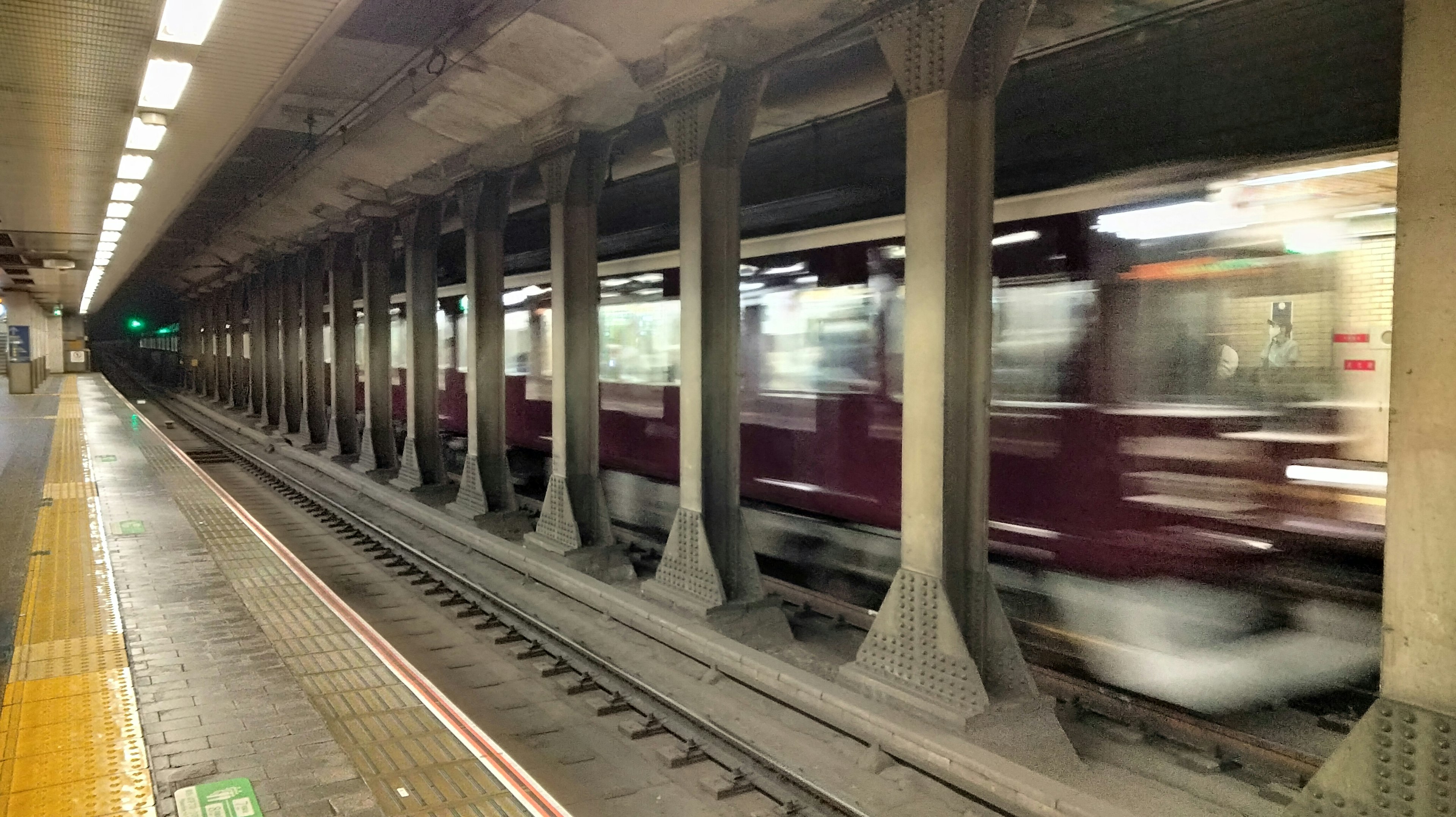 Subway station platform with a train in motion and distinctive columns