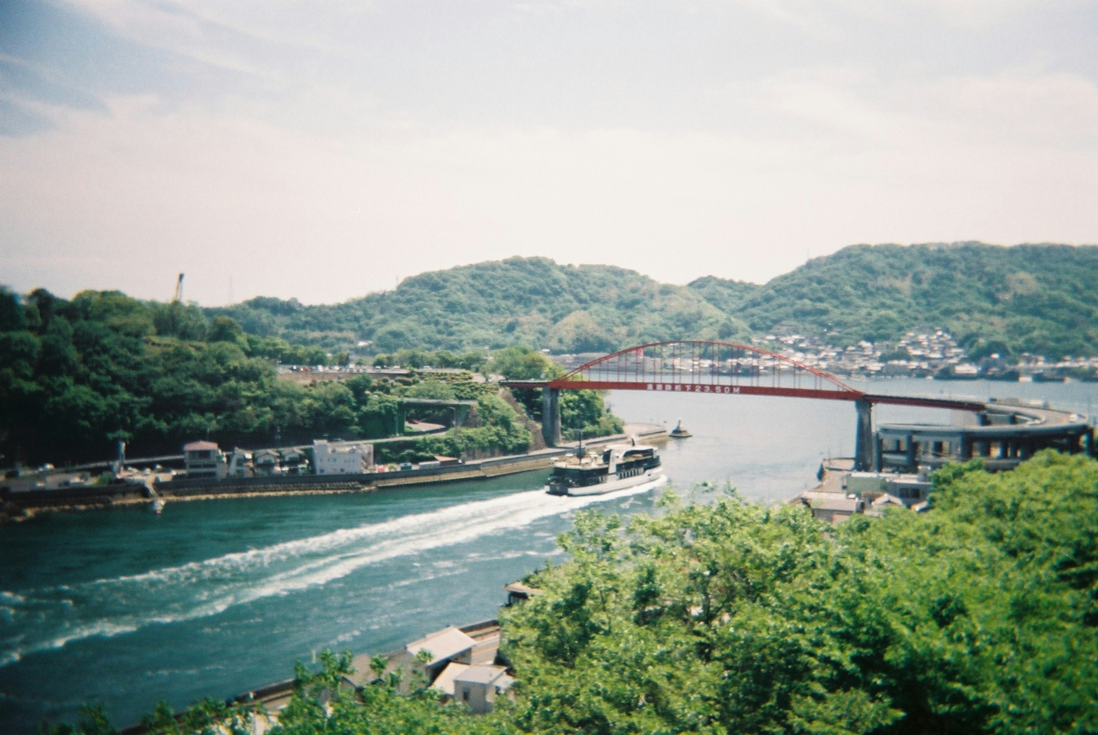 Malersicher Blick auf einen Fluss mit üppigen grünen Hügeln und einer roten Brücke Ein Boot fährt auf dem Wasser