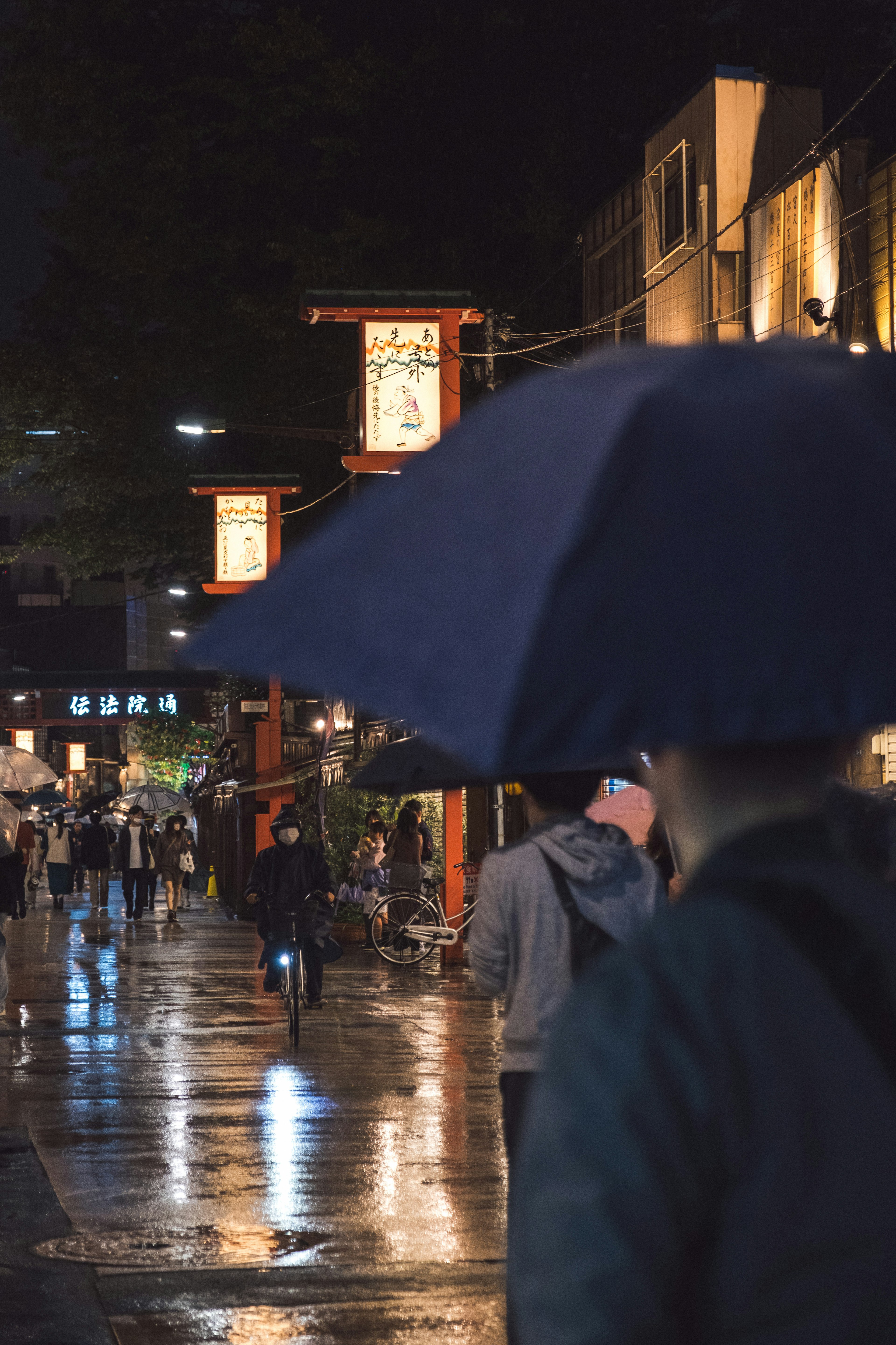 คนที่ถือร่มในถนนที่มีฝนสะท้อนแสงไฟในยามค่ำคืน