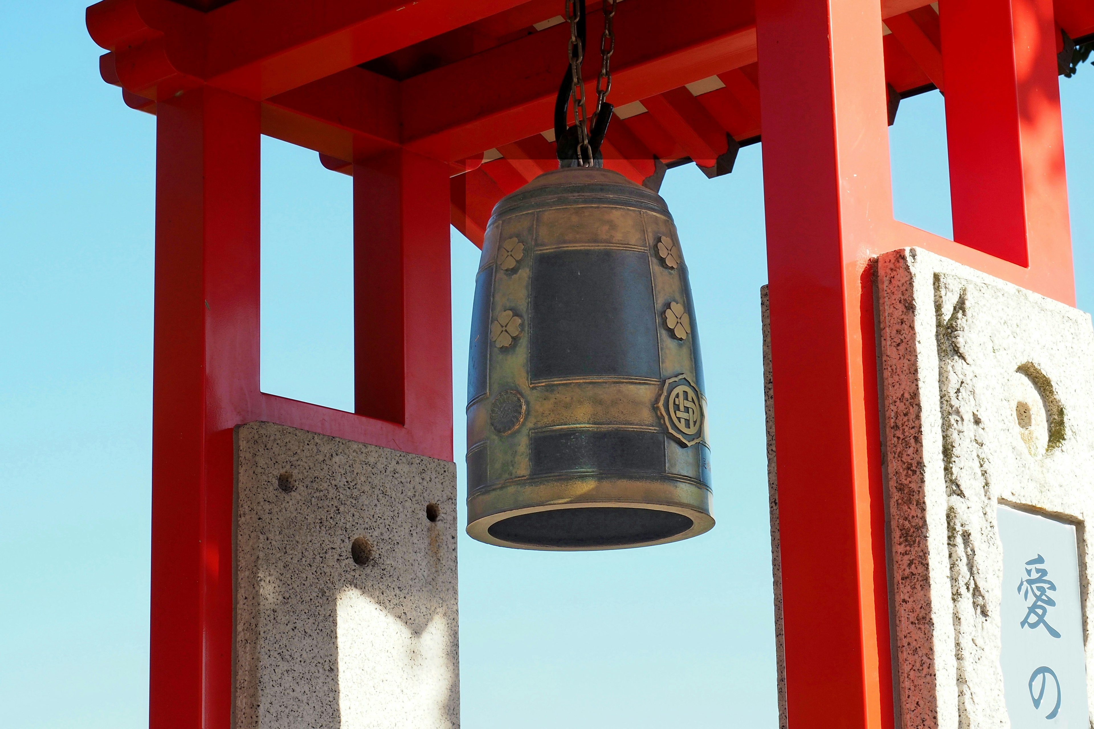 Cloche suspendue sous un torii rouge avec un ciel bleu