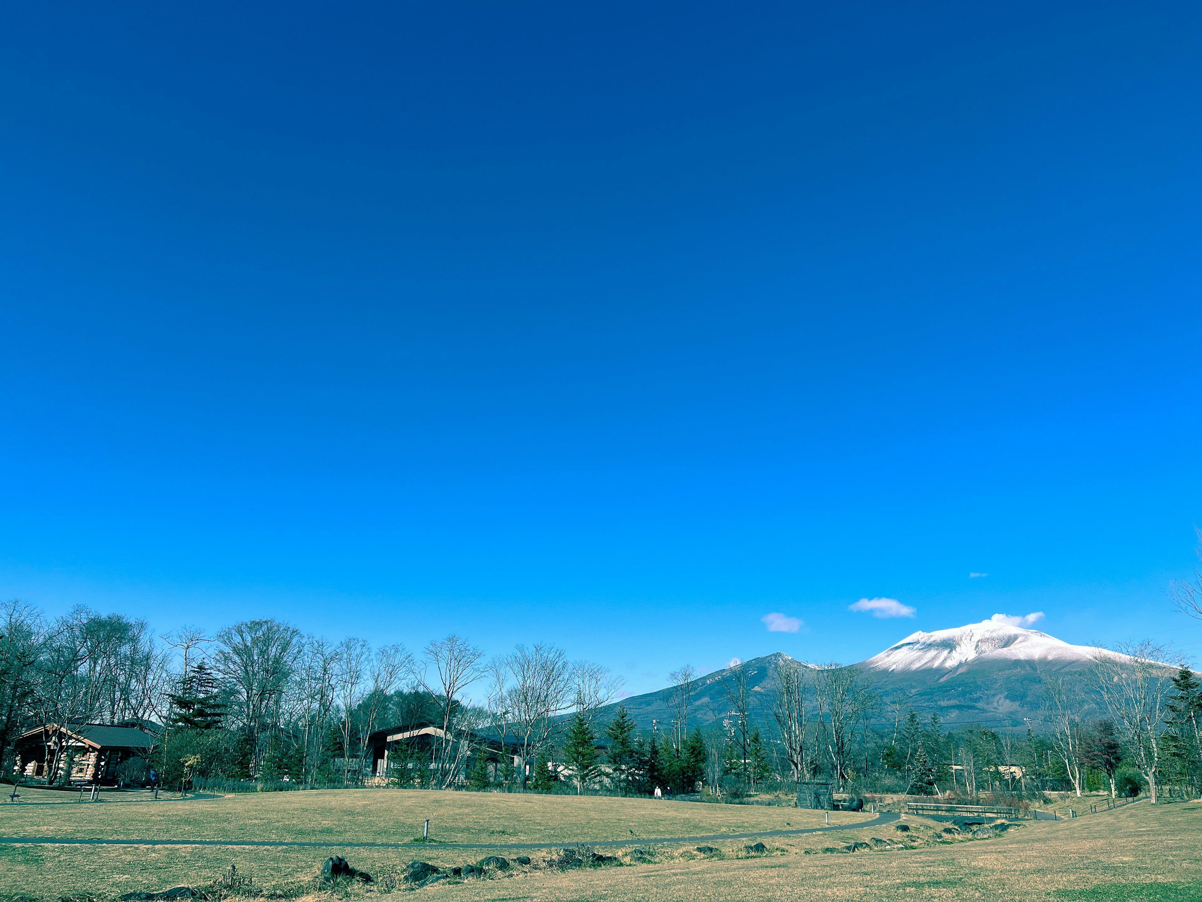 青空と雪をかぶった山が見える景色 いくつかの小屋と木々が周囲に点在