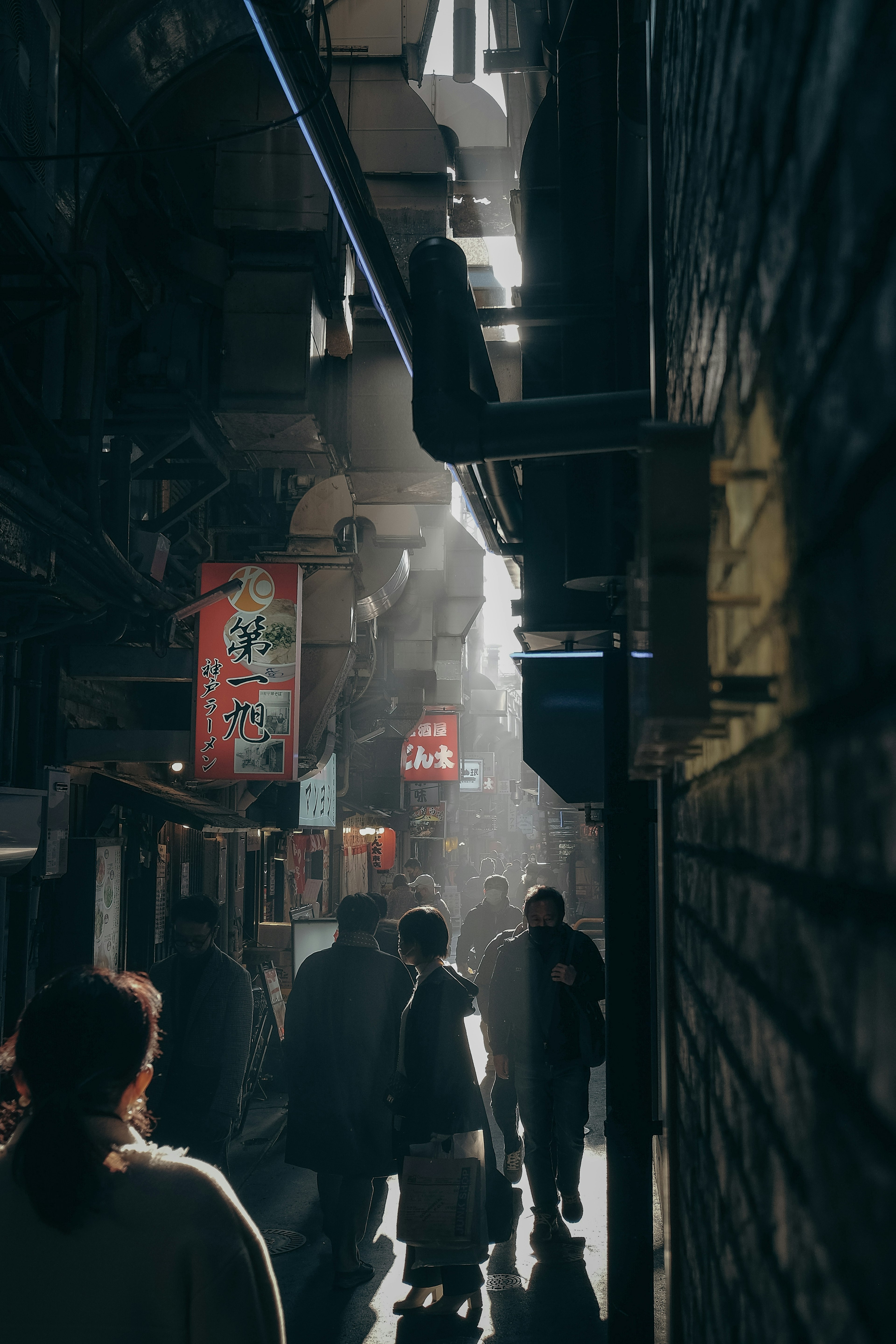 People walking through a dim alley with beams of light shining through