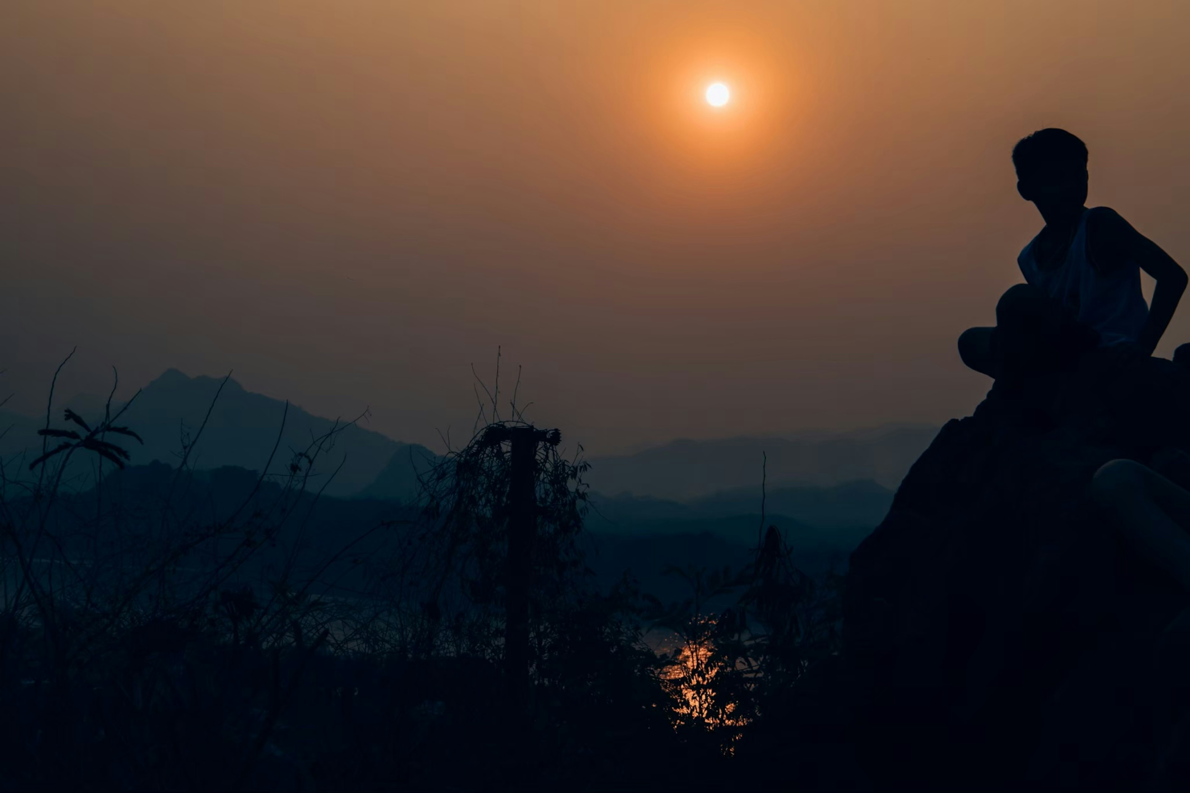 夕日を背景に座る少年のシルエットと静かな風景