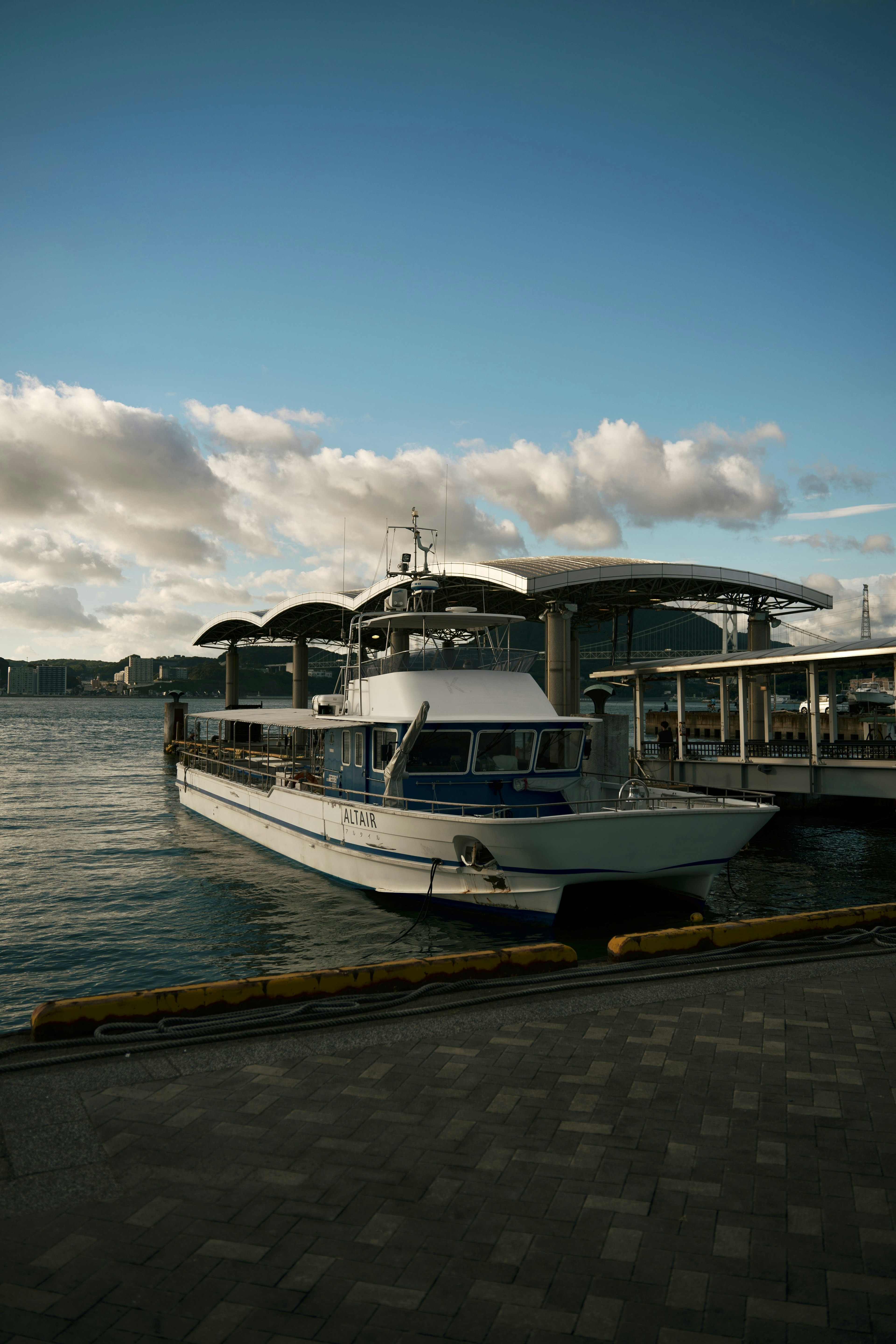 Ein weißes Boot unter einem blauen Himmel mit Wolken und einem nahegelegenen Pier